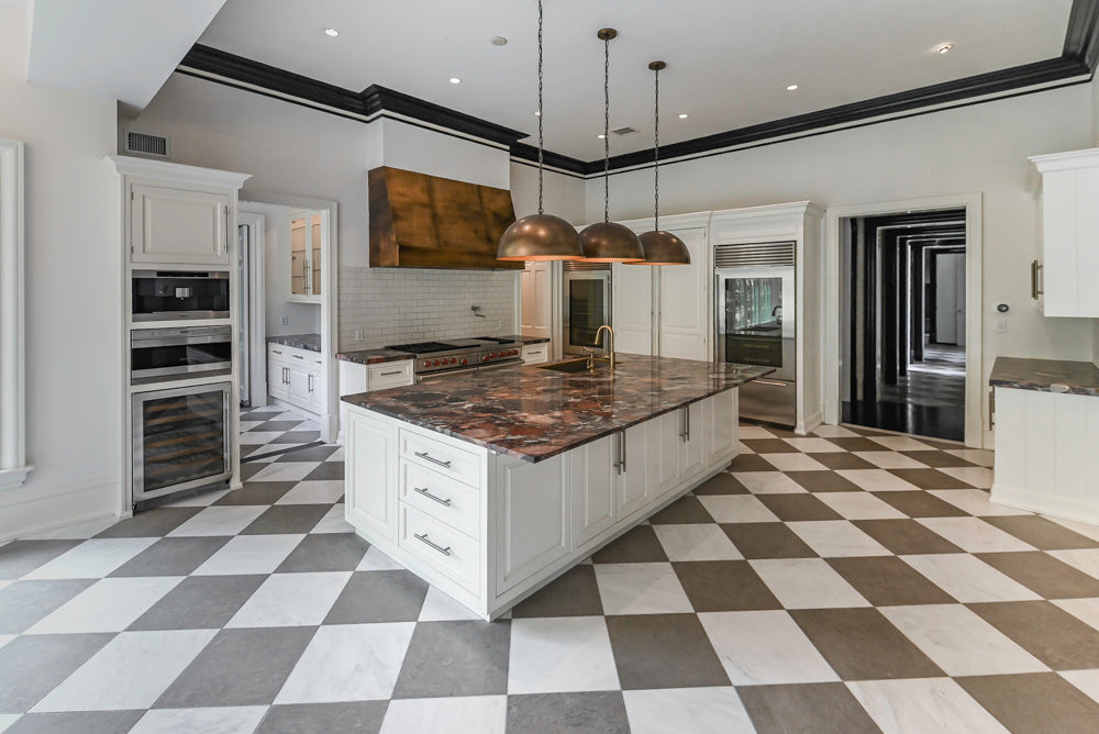 Luxury kitchen renovation featuring white cabinetry, a large marble island and black-and-white tiled flooring.