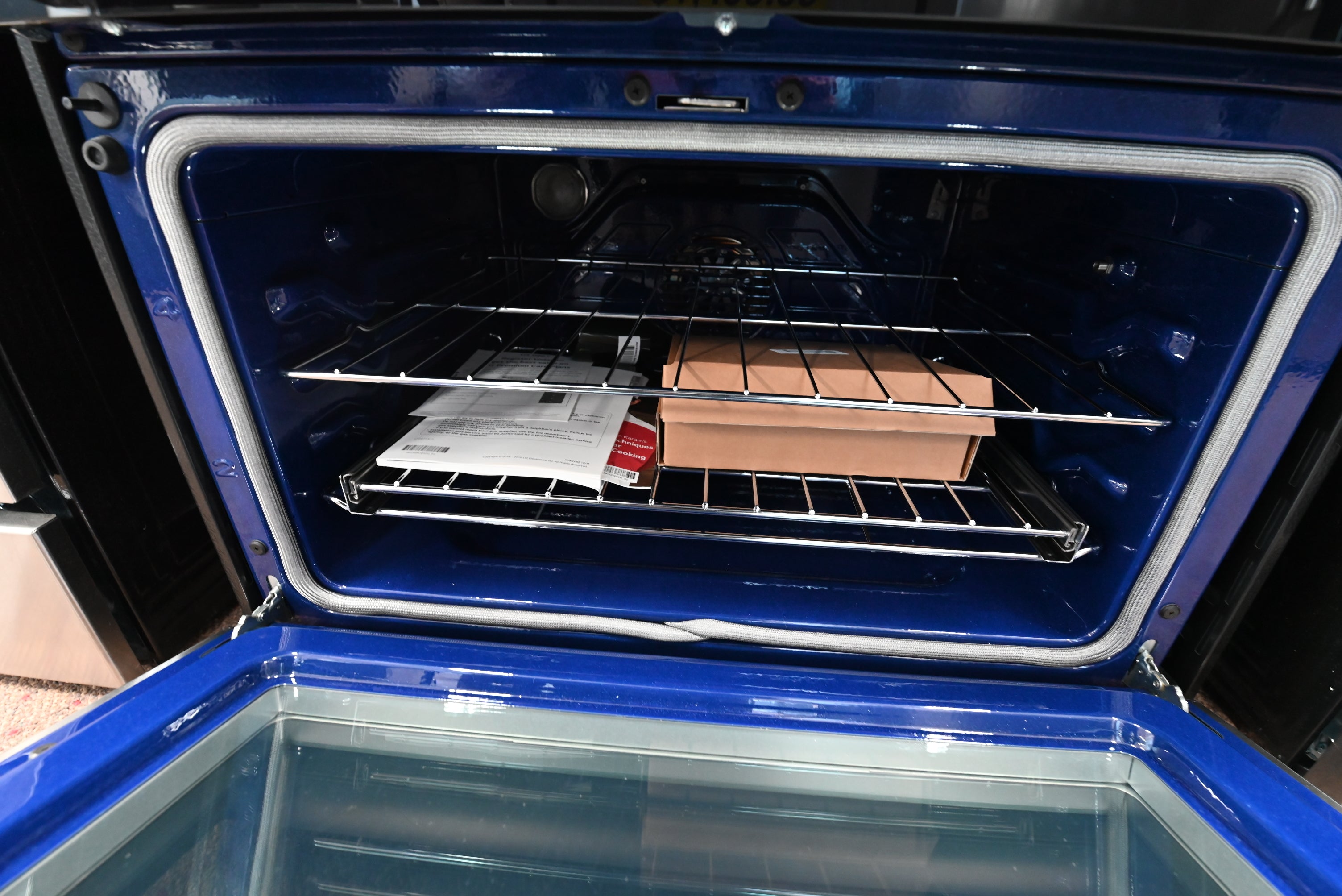 An open blue oven with wire racks, showing a brown rectangular item and some papers inside.