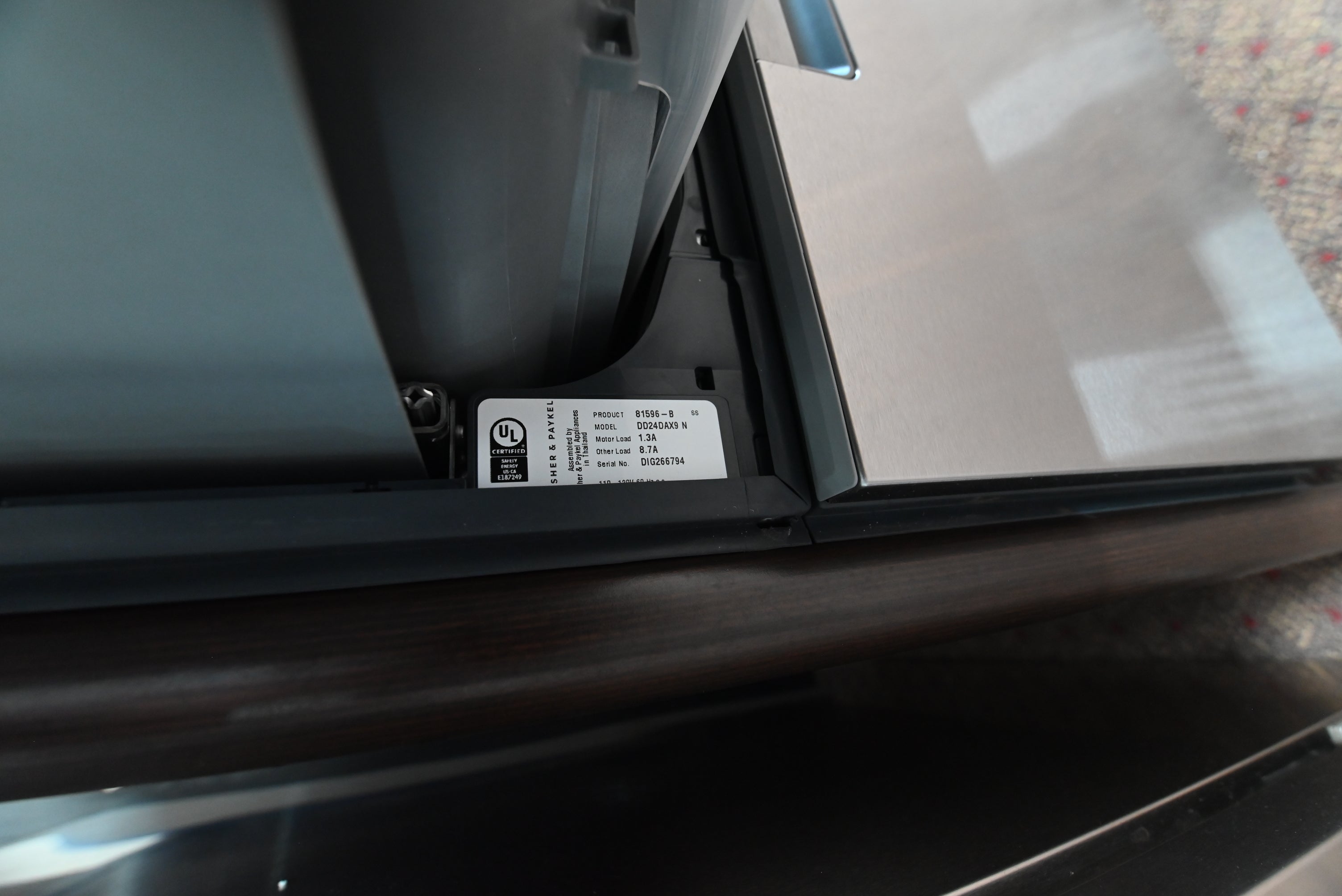 Close-up of the lower edge of a dark gray appliance, showing a white UL certification label attached to the black trim.
