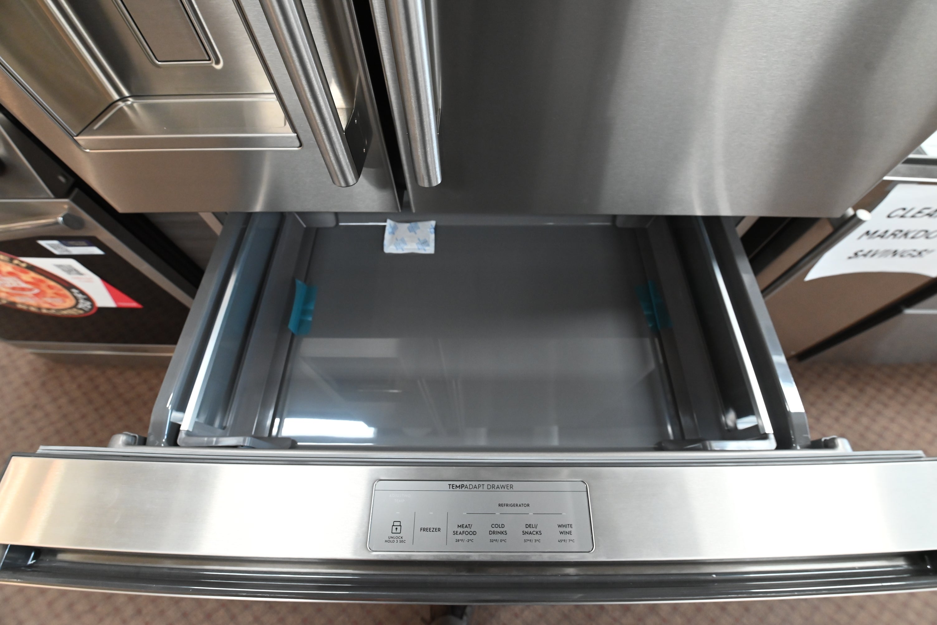 A close-up of a stainless steel refrigerator drawer pulled open, showing the interior and a control panel on the front.