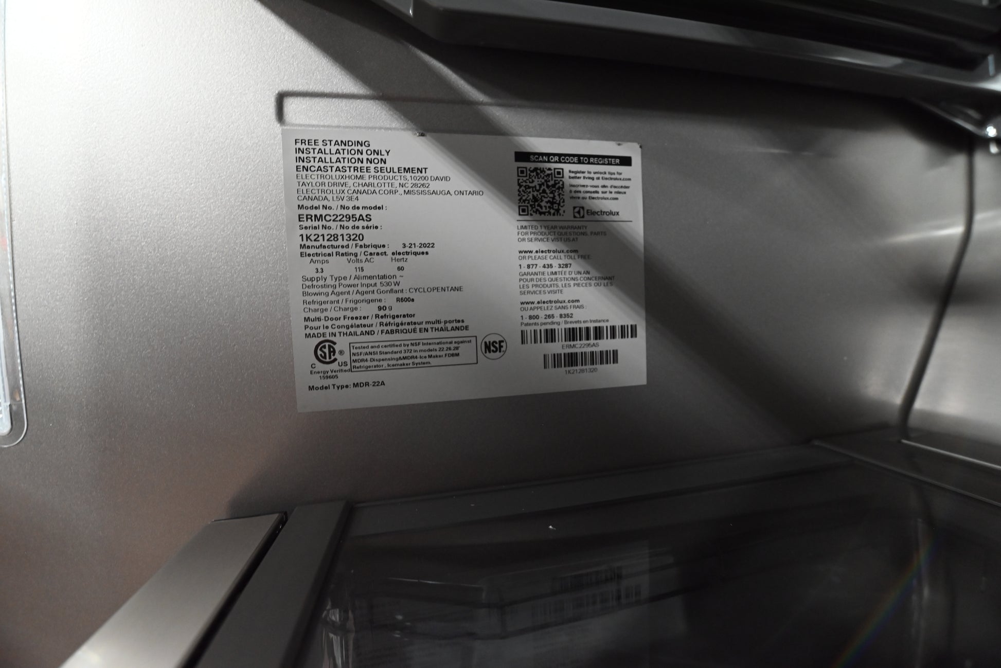 A close-up of a white product information label and barcode sticker applied to the inside of a stainless steel appliance door.