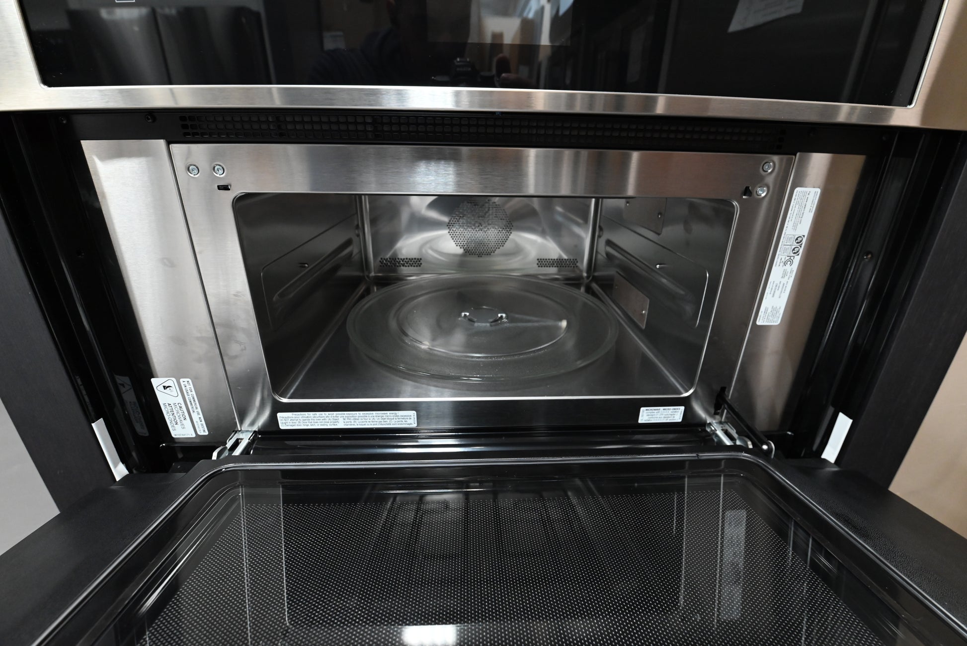 Open doors of a JennAir RISE JMW2430LL wall oven showing black obsidian cavity with bright lights and roll out racks