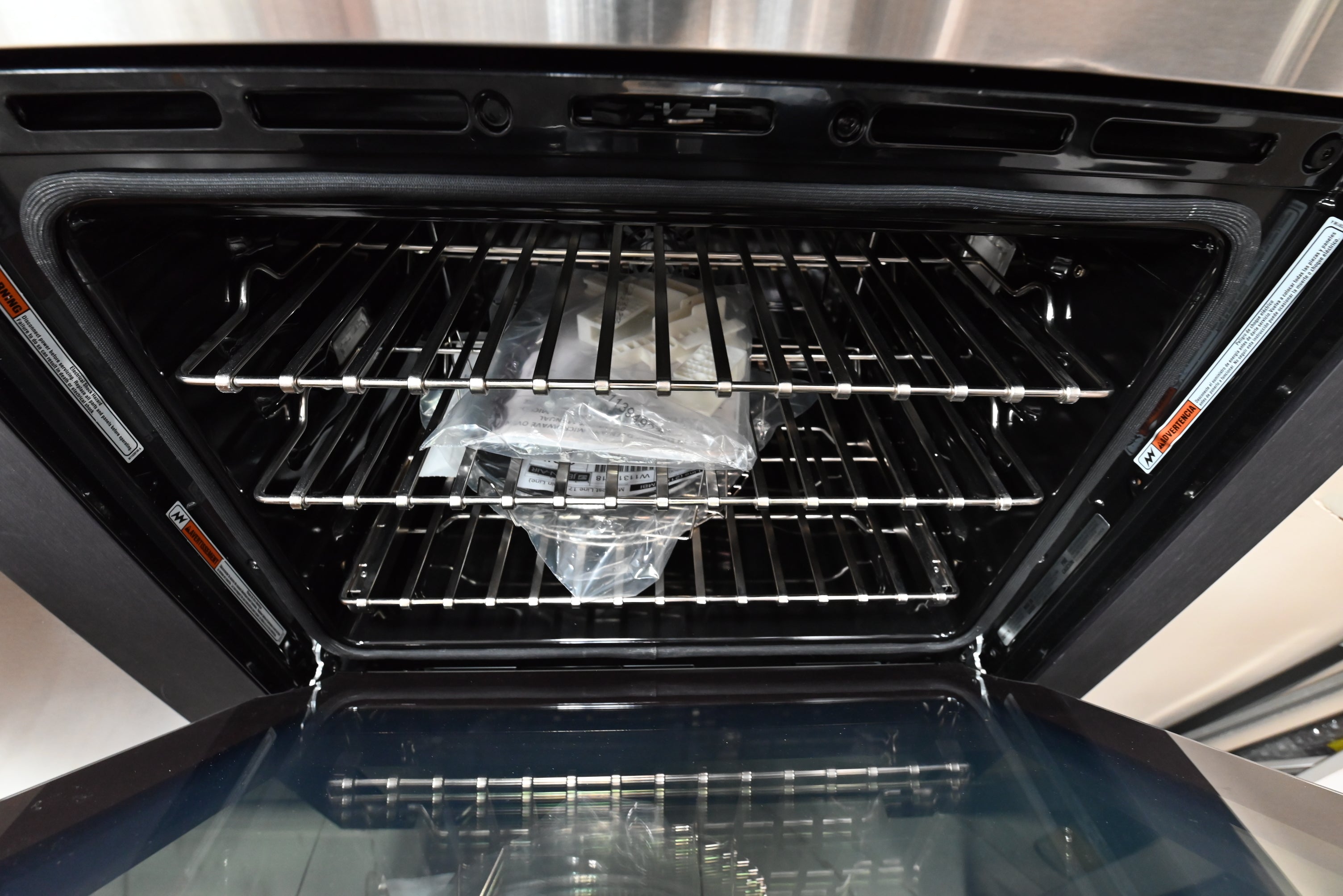 Open black oven door showing interior racks and a clear plastic bag inside, photographed in a real kitchen-like environment.