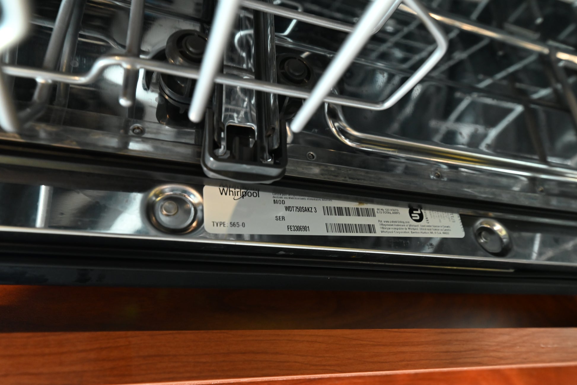 Close-up of a Whirlpool dishwasher interior showing the metal tub rim, spray arms, and a product label sticker on the bottom panel.