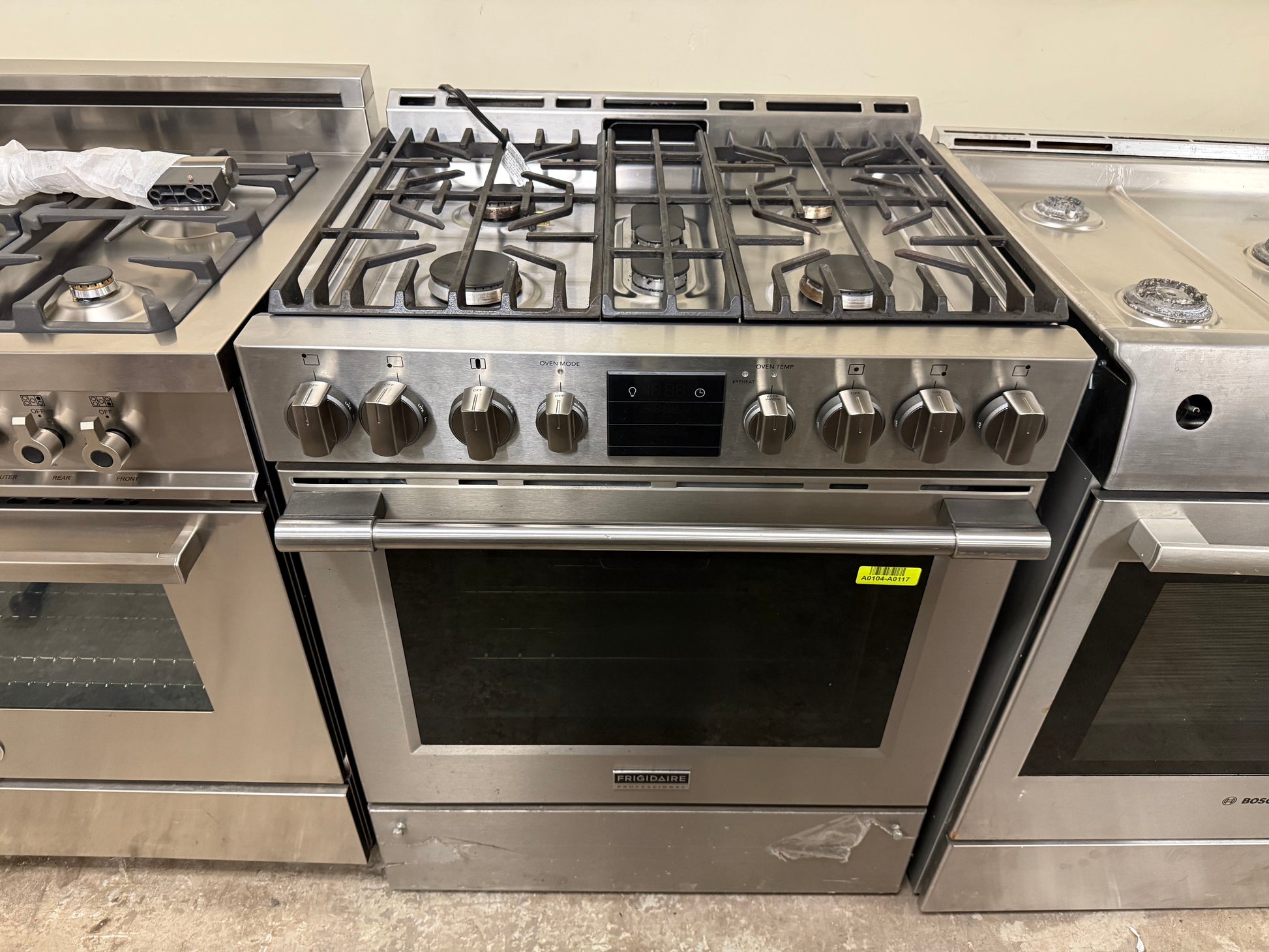 Stainless steel gas stove with multiple burners and control knobs in a showroom setting.