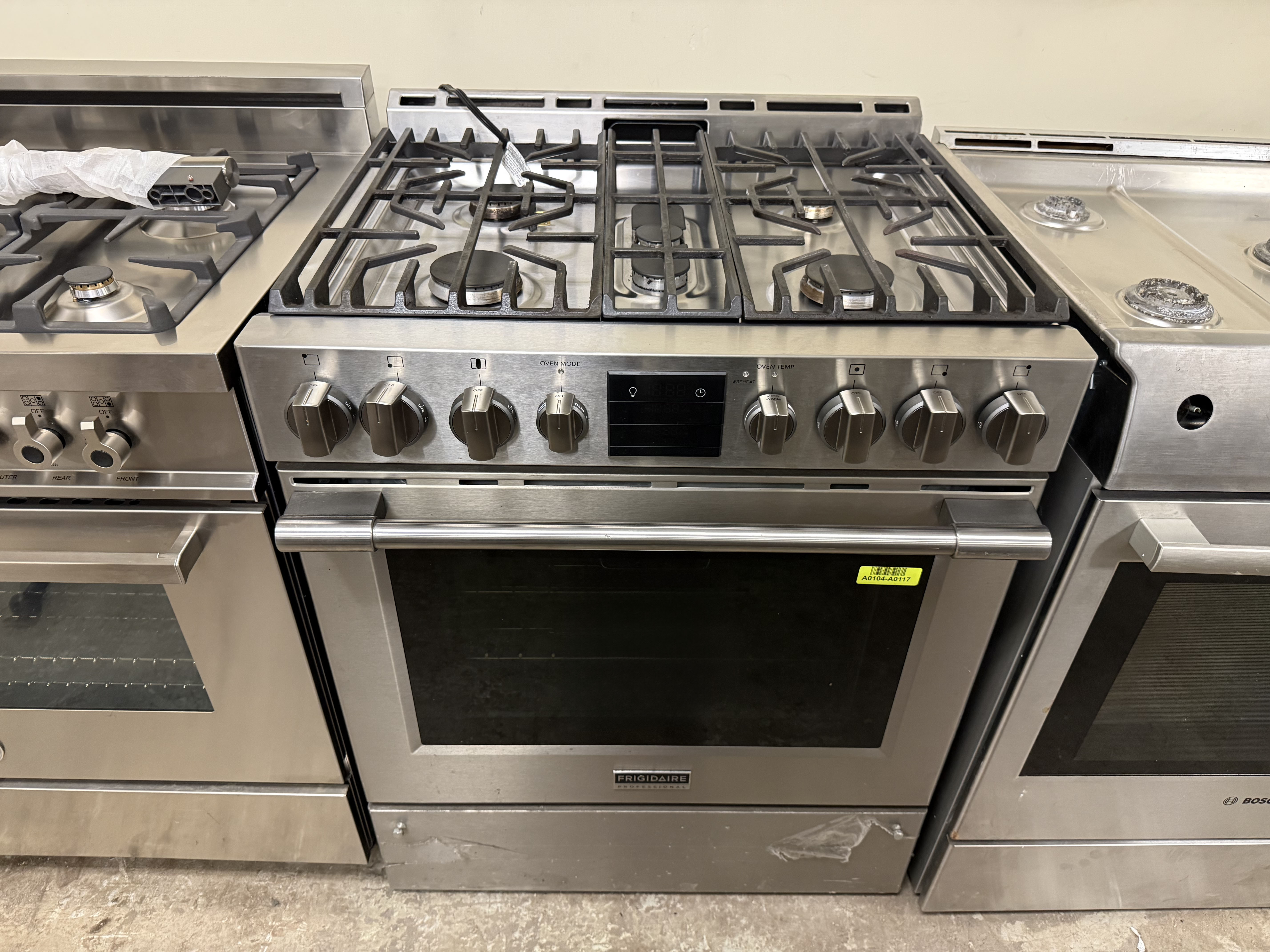 Stainless steel gas stove with multiple burners and control knobs in a showroom setting.