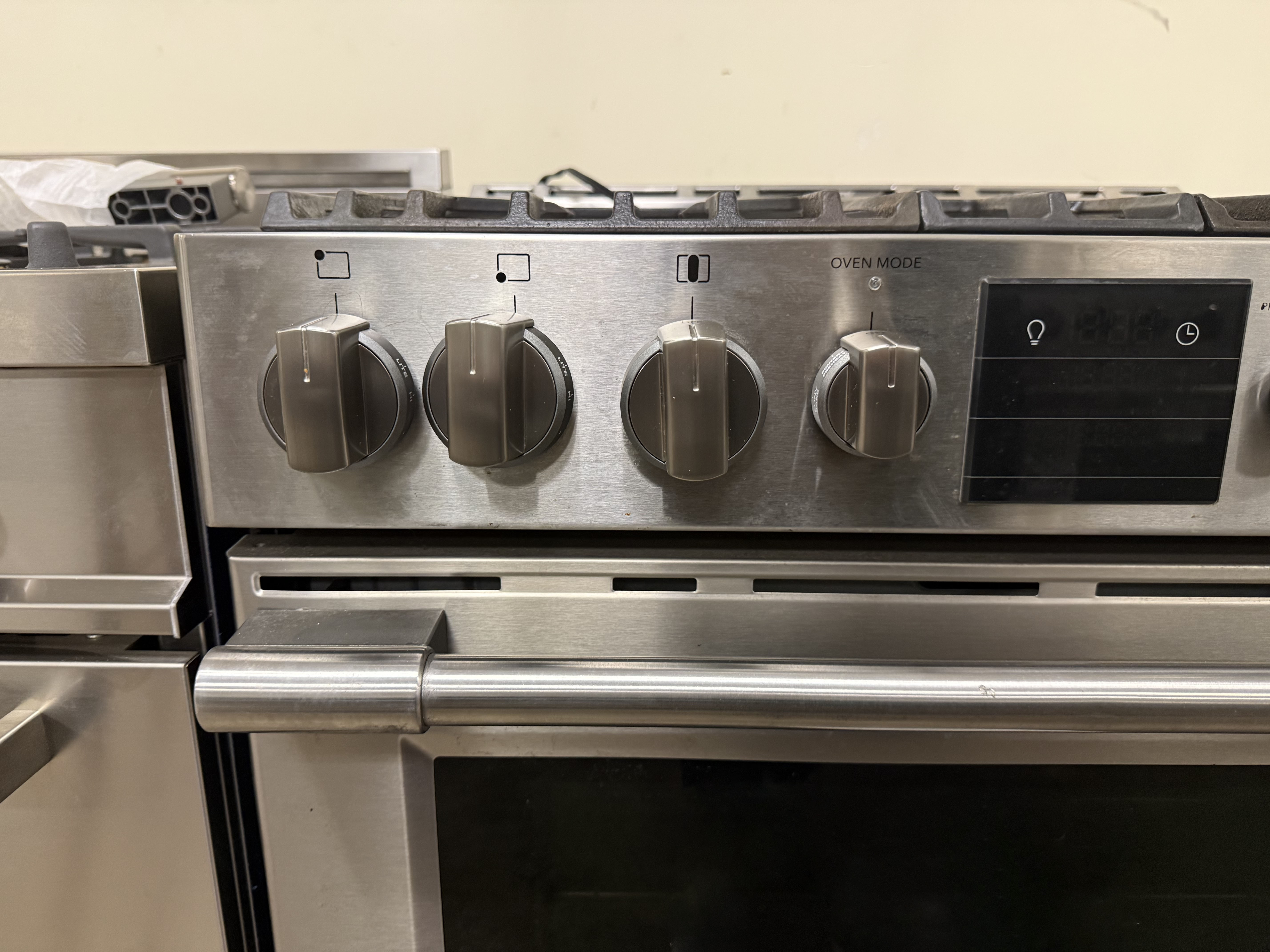 Stainless steel oven with control knobs on a beige wall background