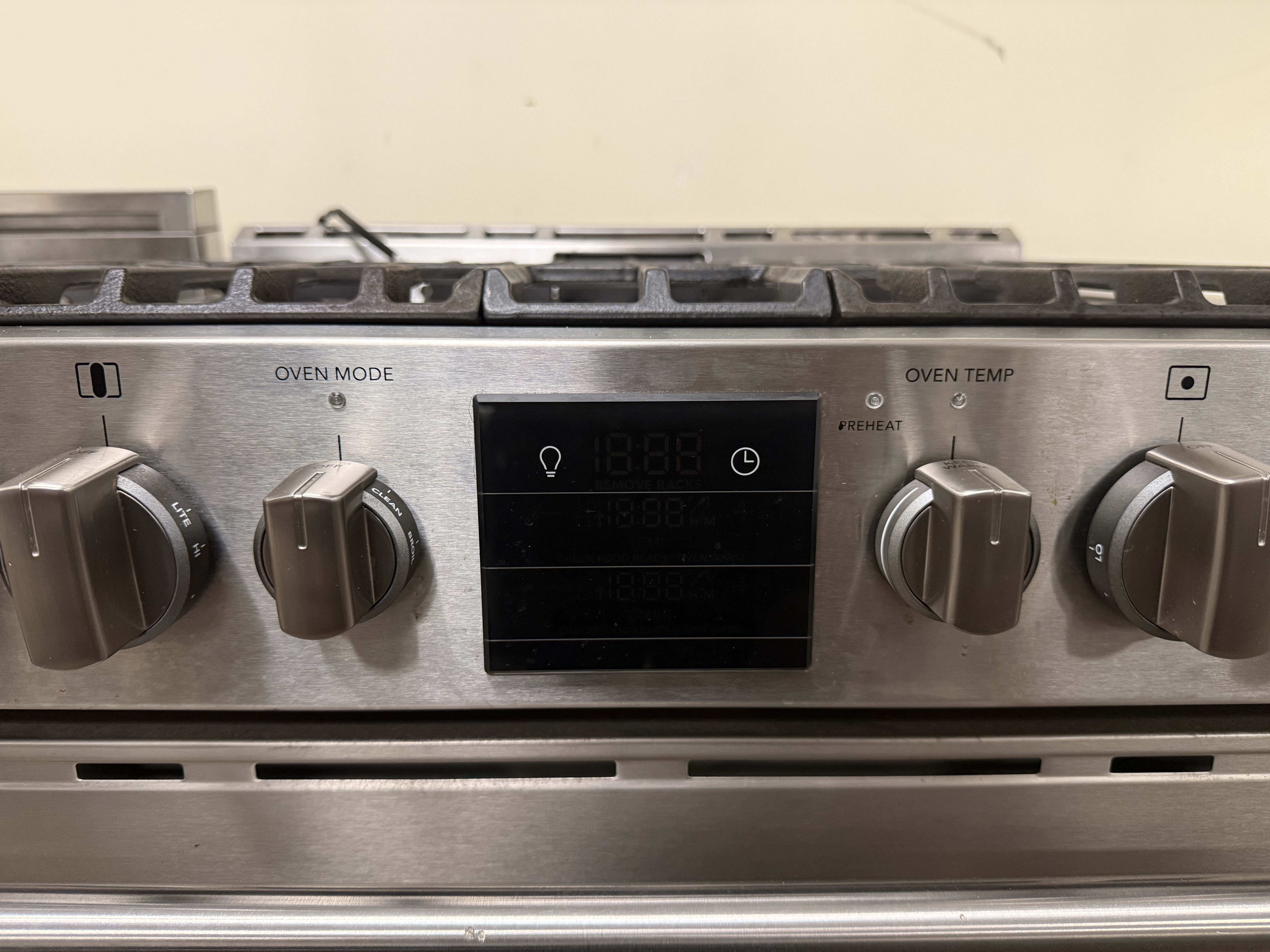 Stainless steel gas stove with control knobs and display on a beige background