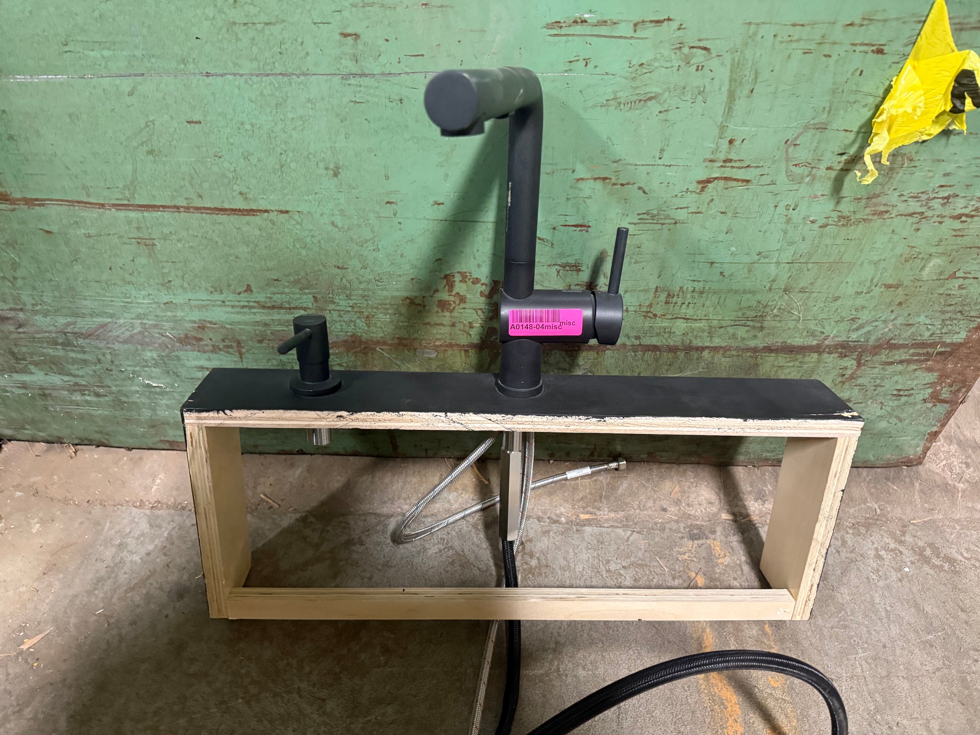 Black faucet on a wooden stand against a green wall.