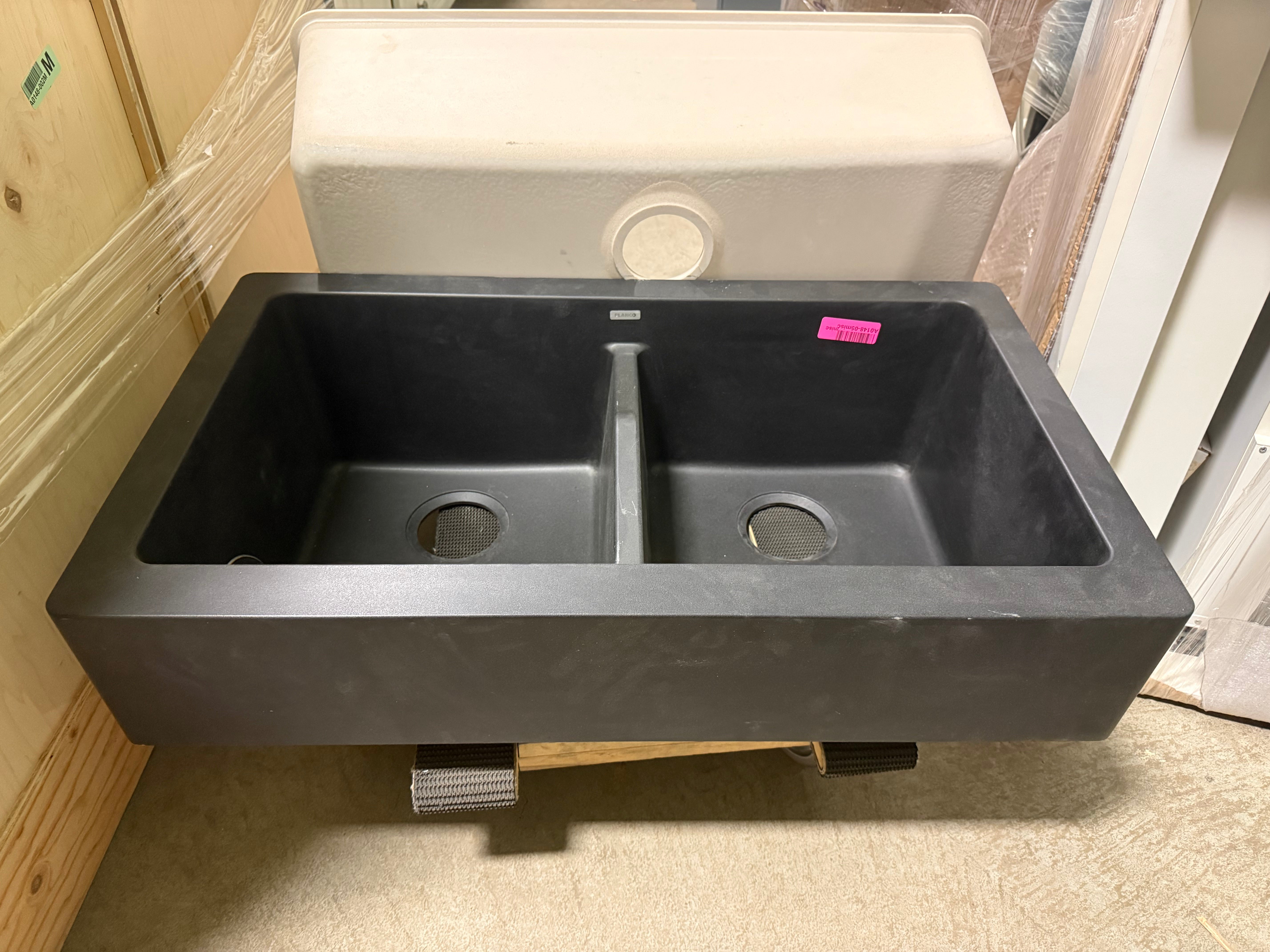 Black double-basin sink on a stand with a pink tag, in a storage or warehouse setting.