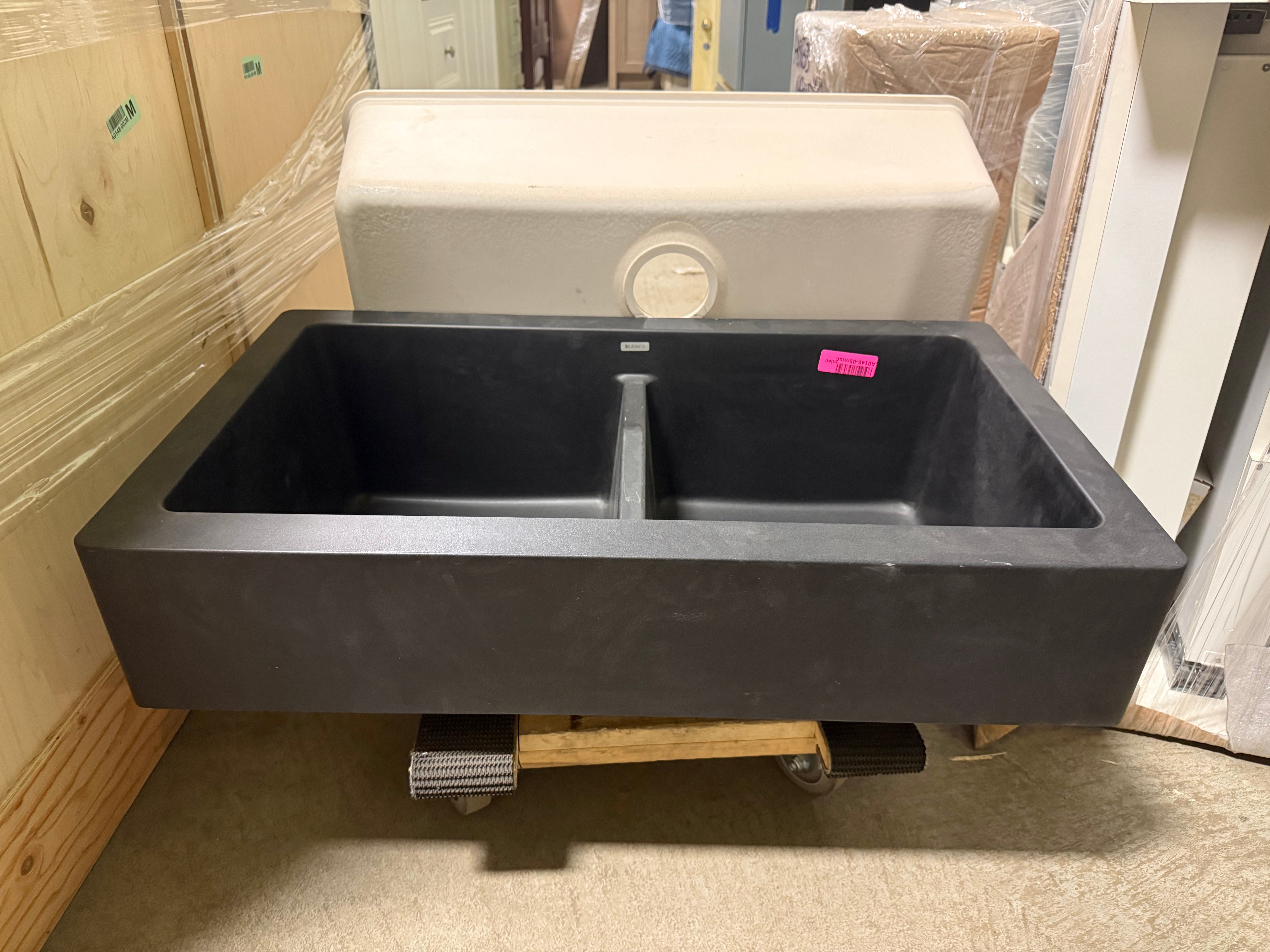 Black double-basin sink on a wooden pallet with a pink tag in an indoor setting.