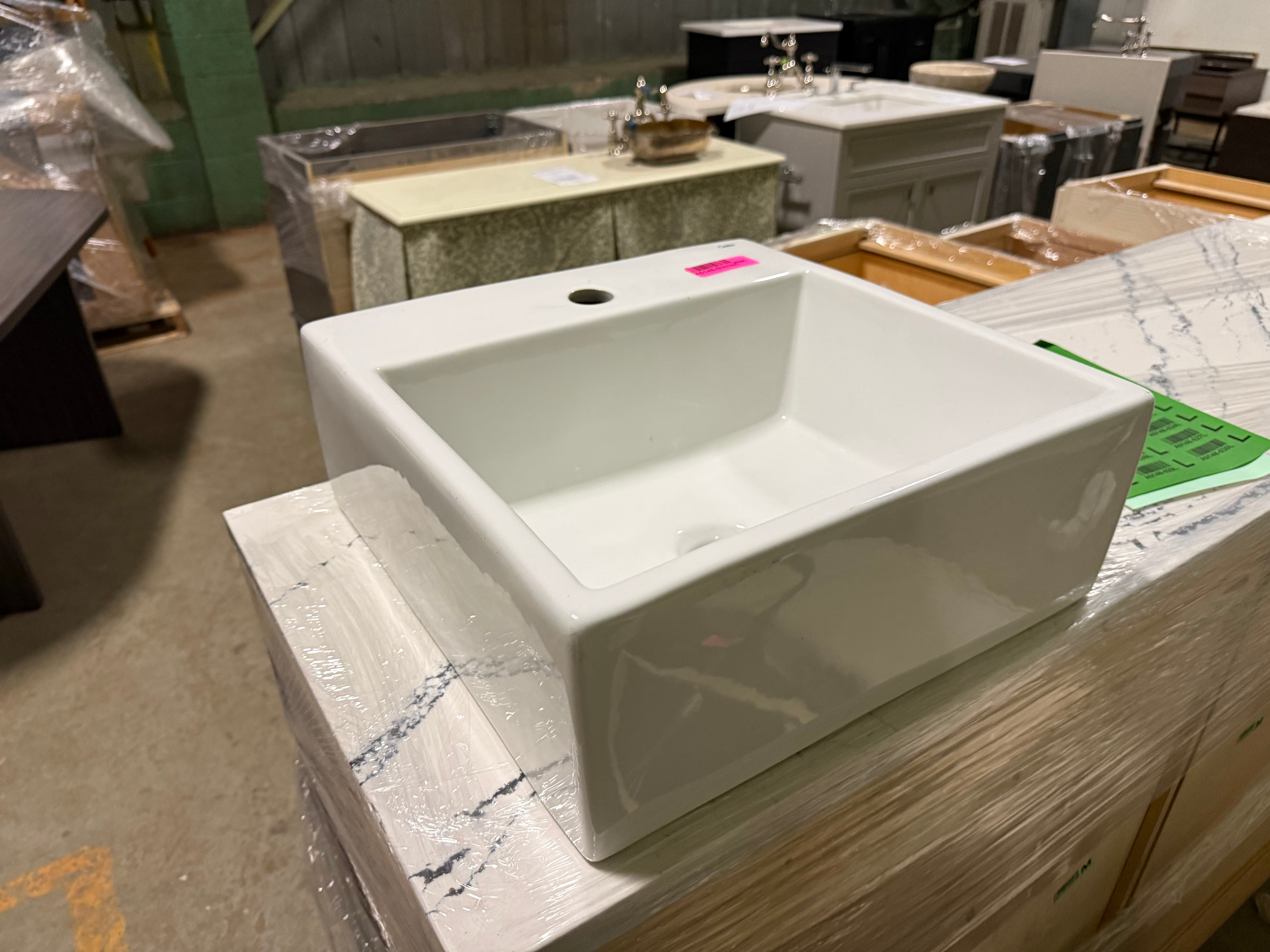White rectangular sink on a wooden surface with a pink tag in a warehouse setting.