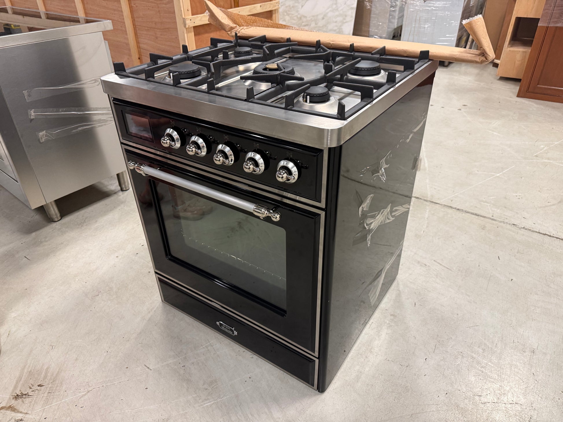 Showroom display ILVE 30 range showing 5 matte black brass burners and continuous iron grates