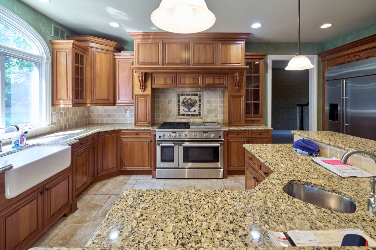 Aurora Circ traditional wood kitchen with raised panel cabinets granite counters farmhouse sink stainless range and tiled backsplash