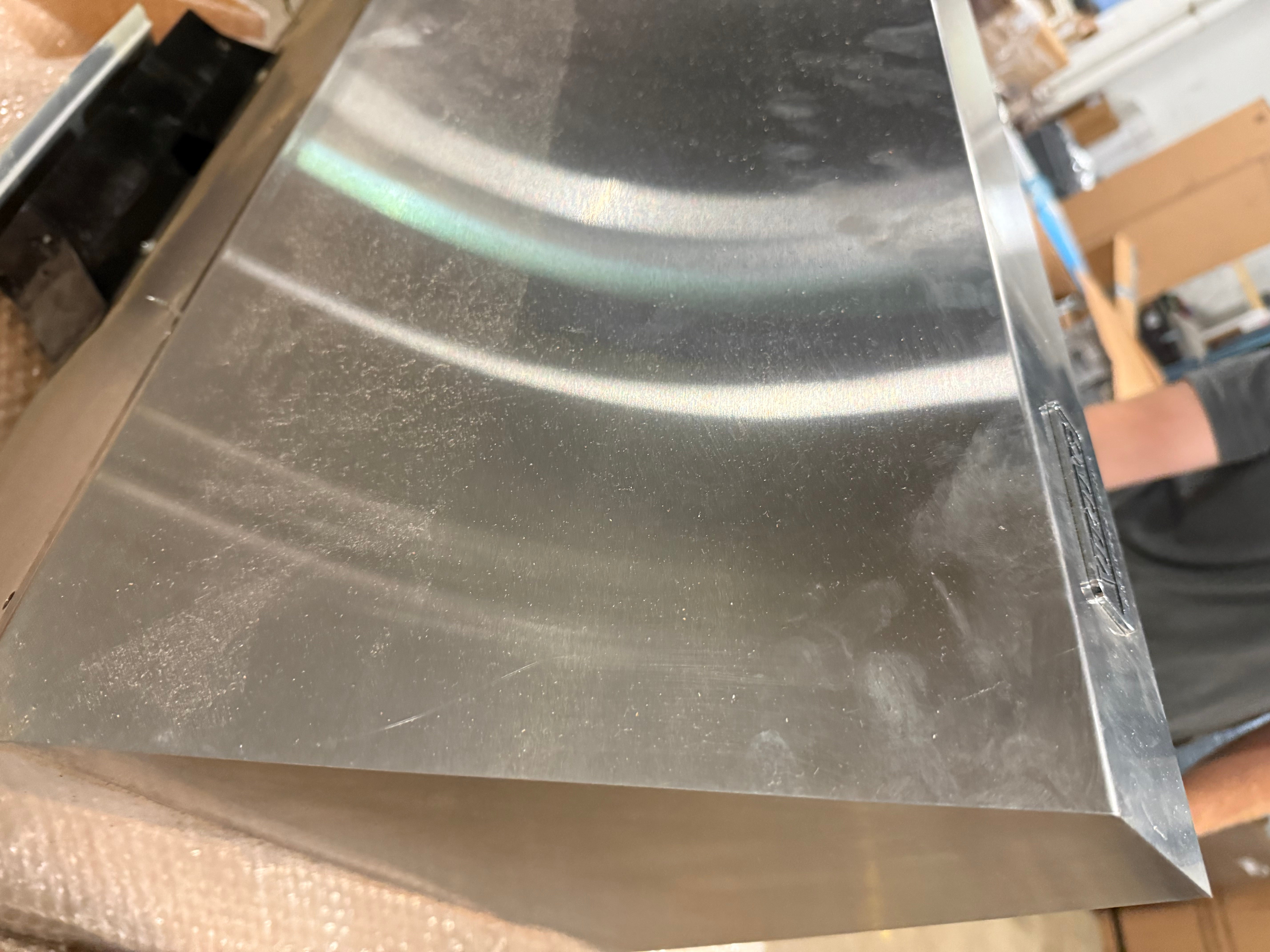 A close-up of a brushed stainless steel panel, likely an appliance component or cabinet front, showing a reflective metallic surface with dust and scratches.