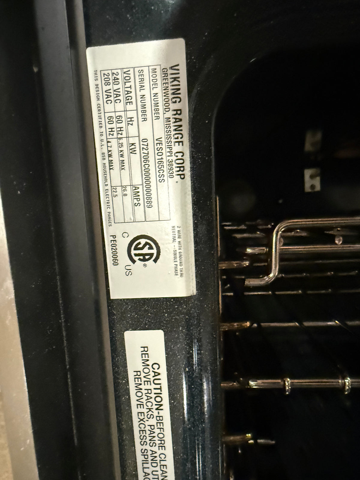 A close-up photo of a Viking Range Corp. appliance label attached to the inside of a dark oven door, showing model information and safety cautions.