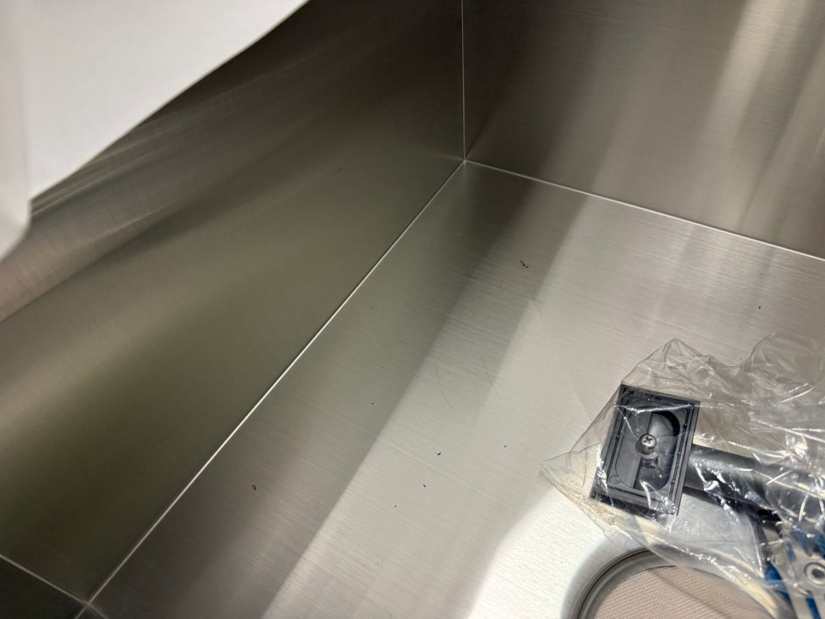 A stainless steel backsplash corner with a small black hardware component in clear plastic packaging on the bottom right.