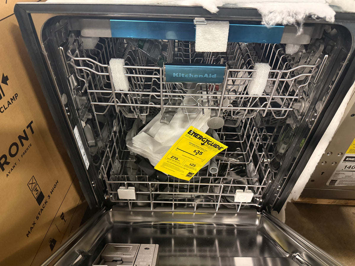 An open KitchenAid dishwasher with stainless steel racks and a yellow Energy Star tag inside, photographed next to its cardboard box.