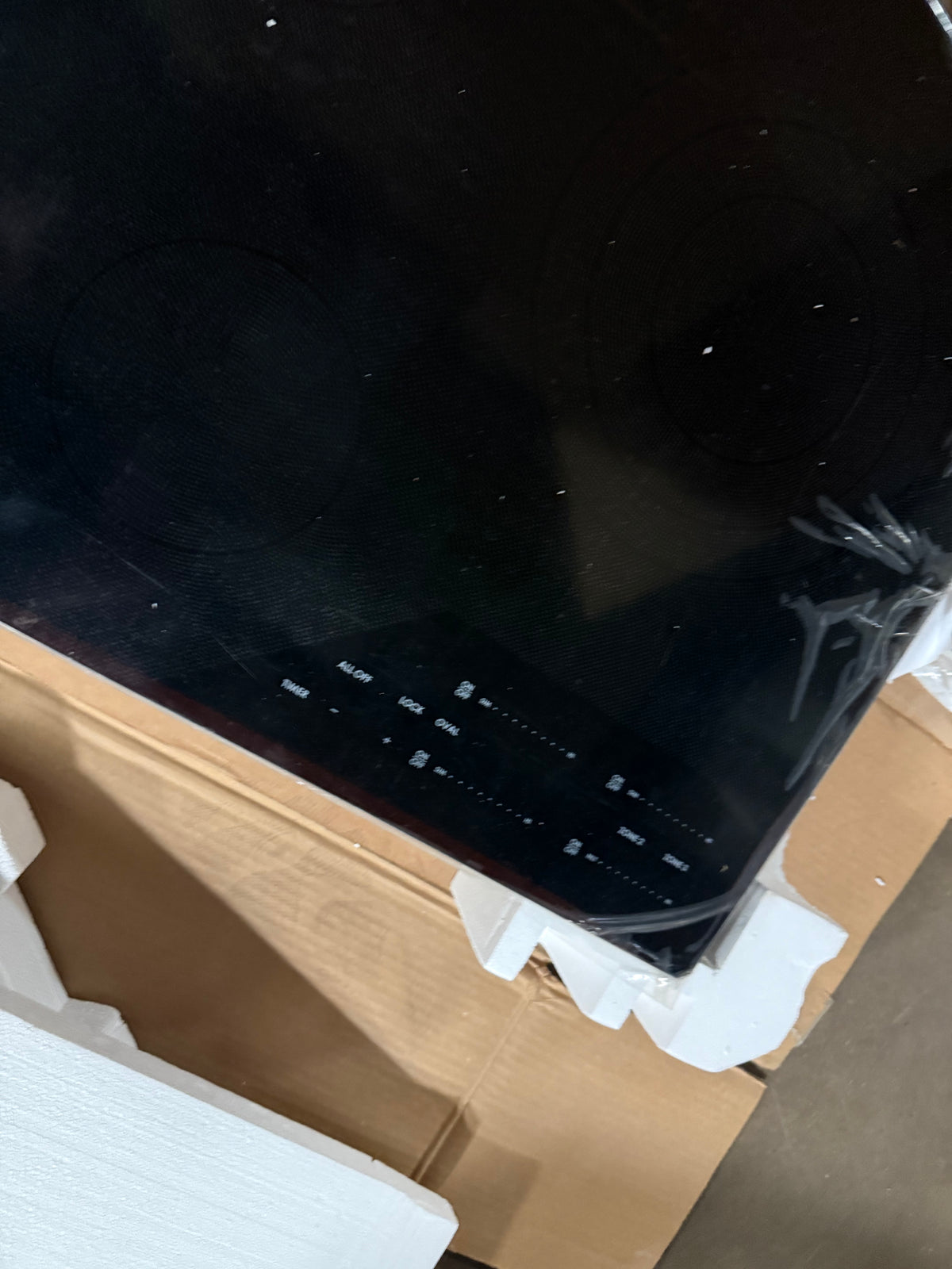 A black glass-ceramic induction cooktop resting on white protective packaging material and a cardboard box.