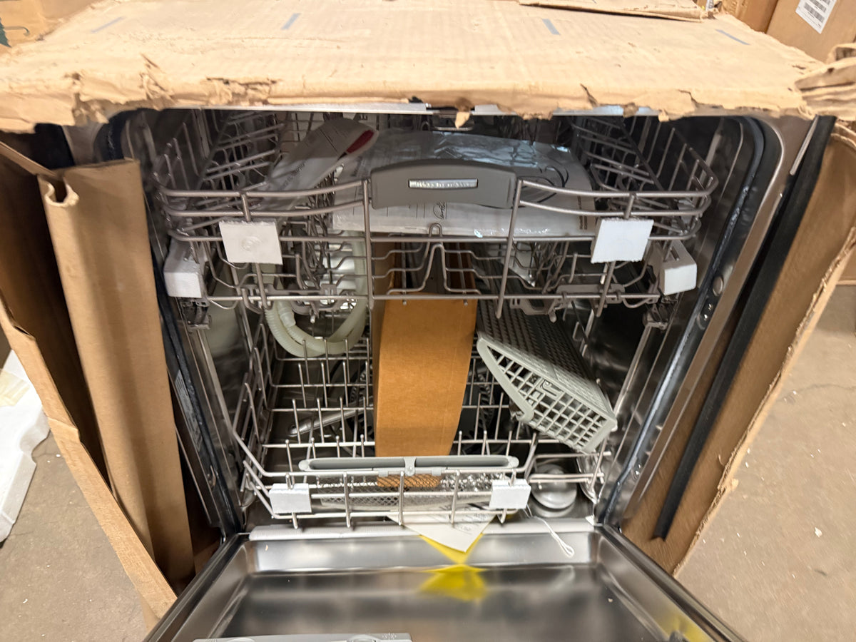 A stainless steel built-in dishwasher with both racks open, showing dirty dishes inside, photographed from above on top of a cardboard box.