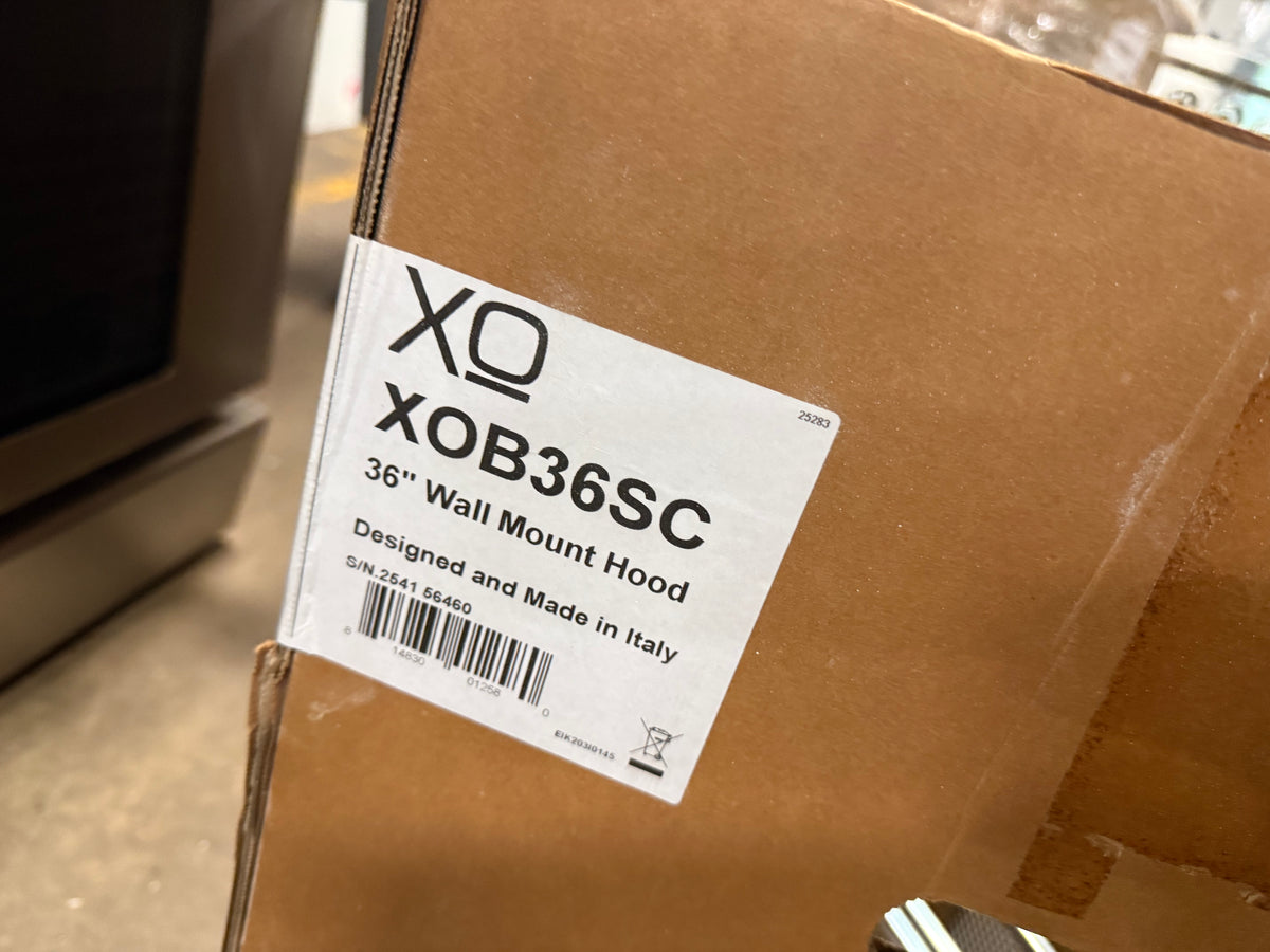 A close-up of a brown cardboard shipping box with a white label reading XQ XOB36SC 36" Wall Mount Hood, photographed in a real indoor environment.