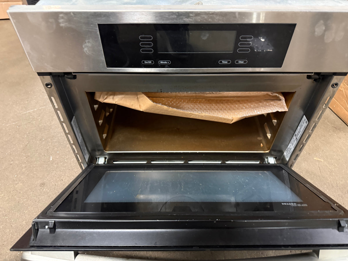 A stainless steel built-in oven with its door open, showing a black glass door, digital control panel, and interior racks with protective paper.