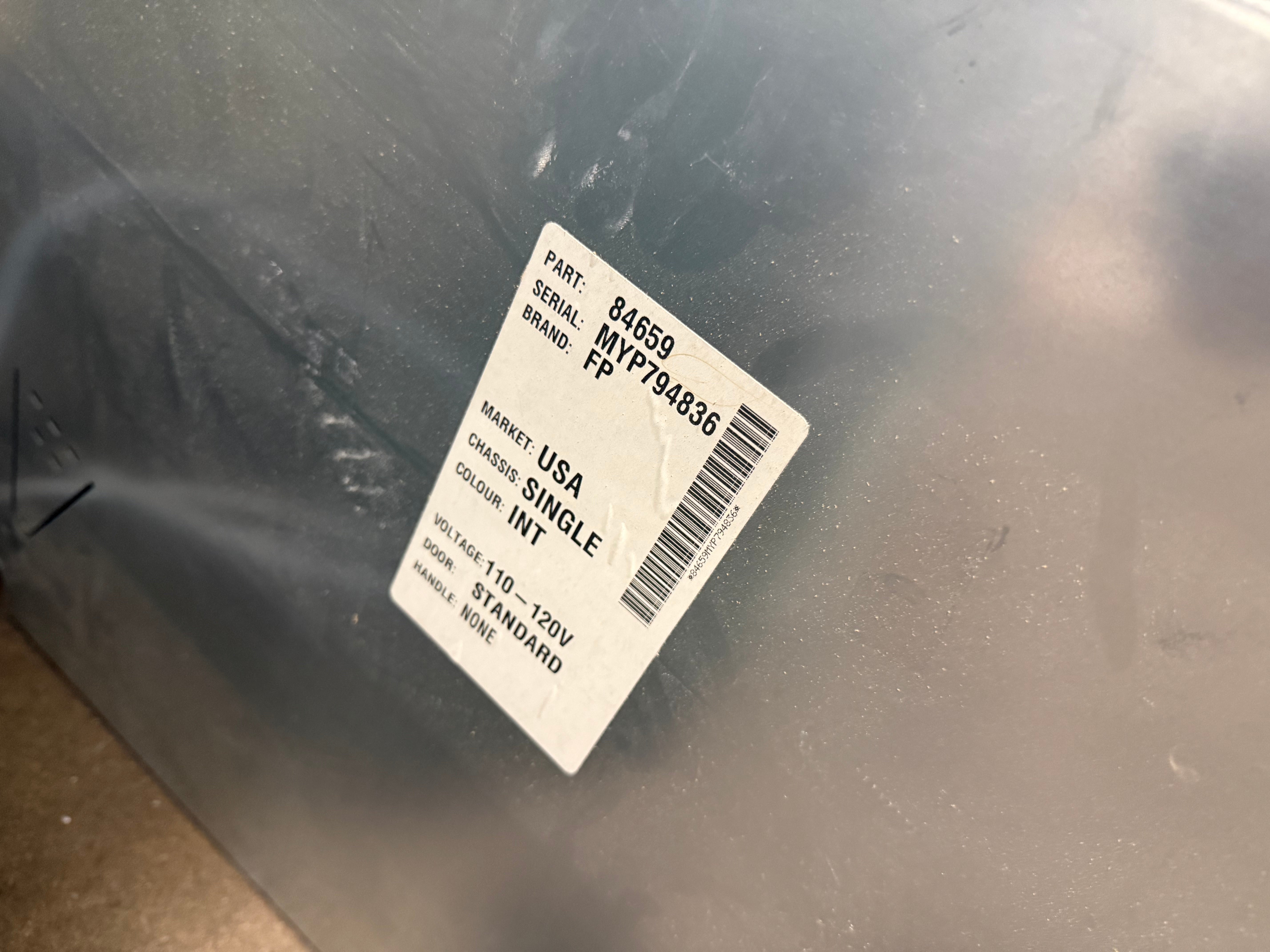 A close-up of a dark gray metallic surface with a white product label that reads 'PART: 846550', 'SERIAL: 0017801836', 'MARKET: USA', 'SINGLE INT', '12V 10A 24V 10AHO', and 'MADE IN USA'.