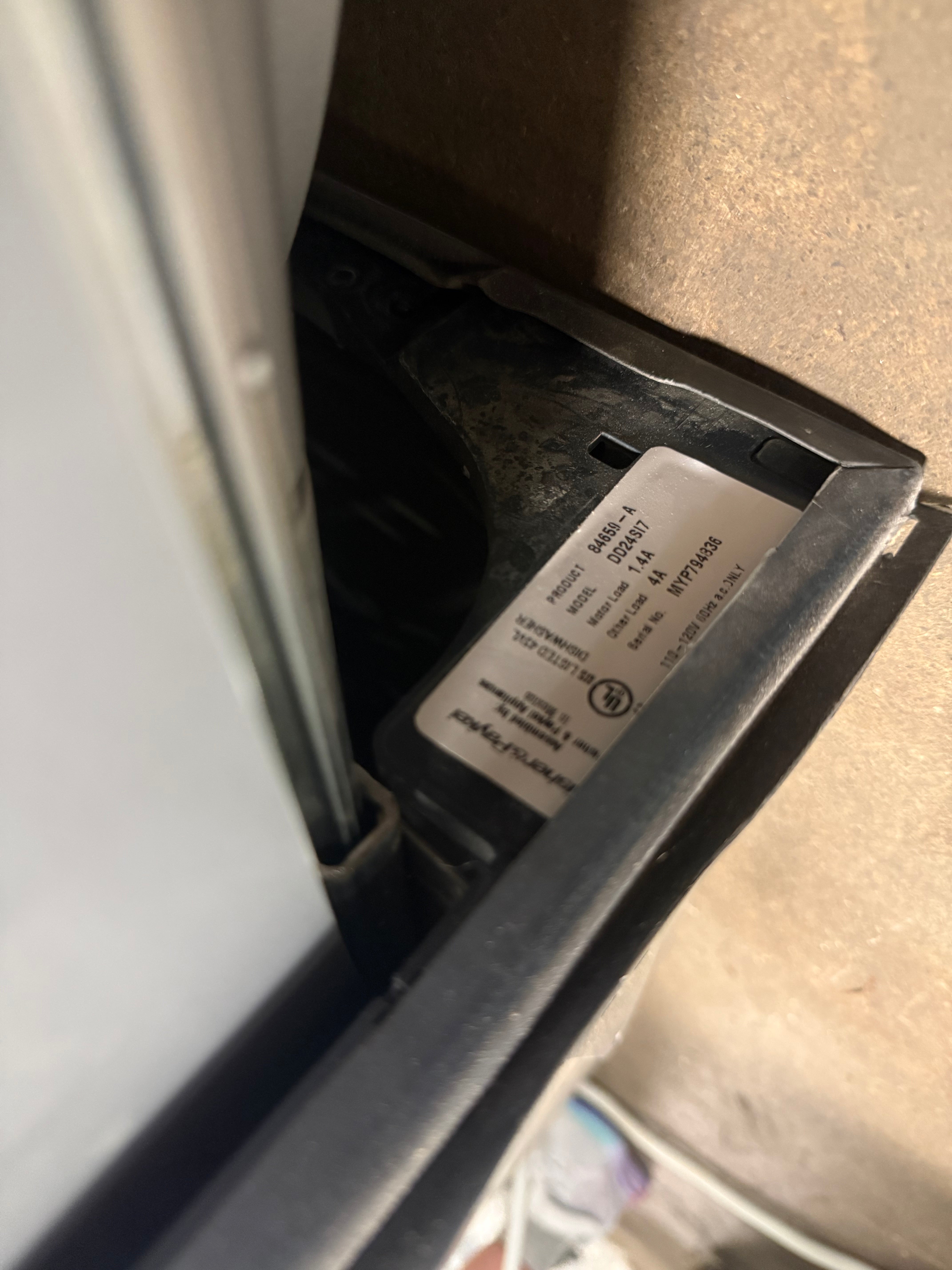 A close-up shot of a black appliance's internal compartment showing a white UL certification label on a beige floor.