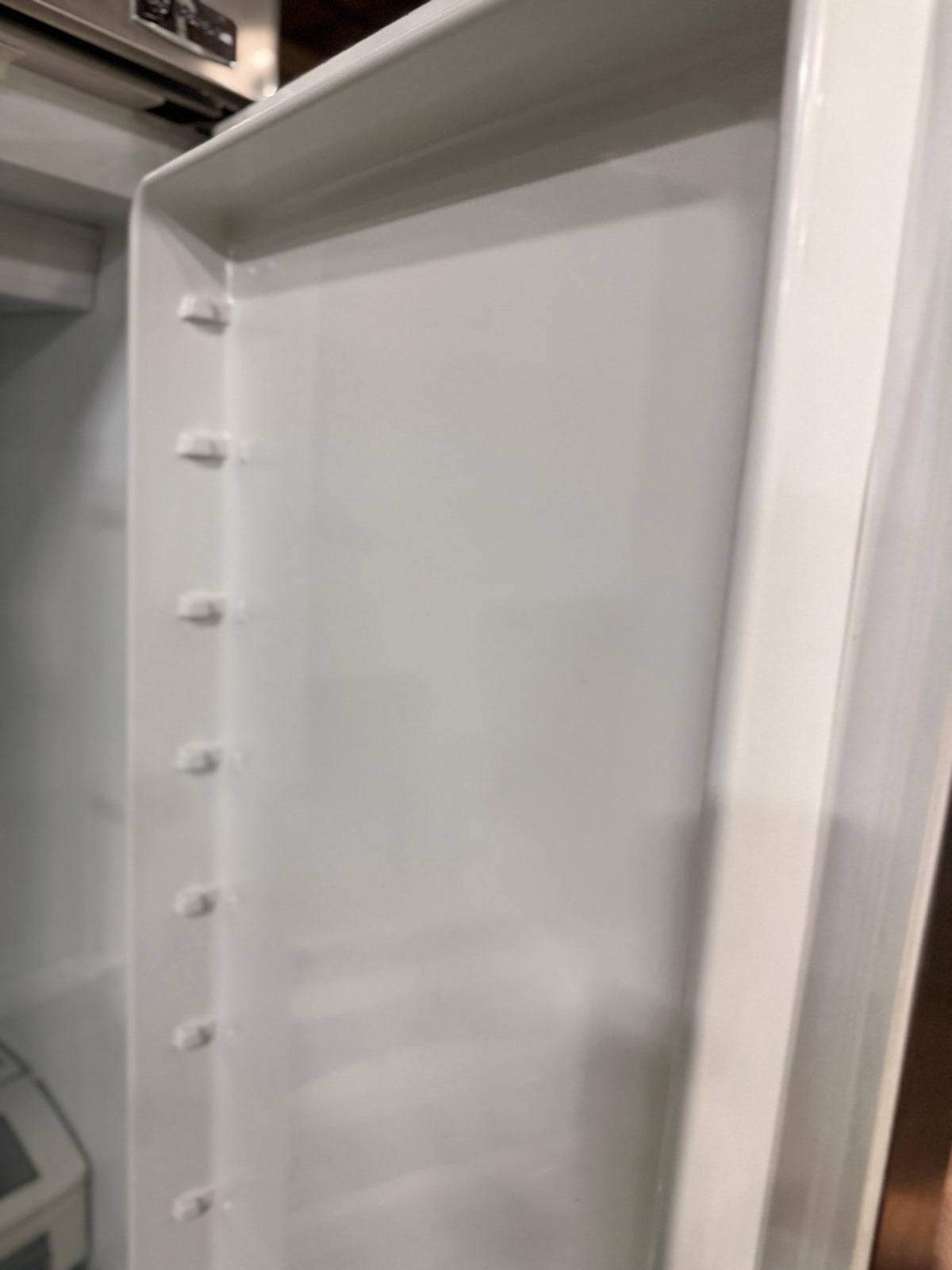 An empty white refrigerator shelf with plastic mounting clips on the left side, photographed inside a refrigerator.