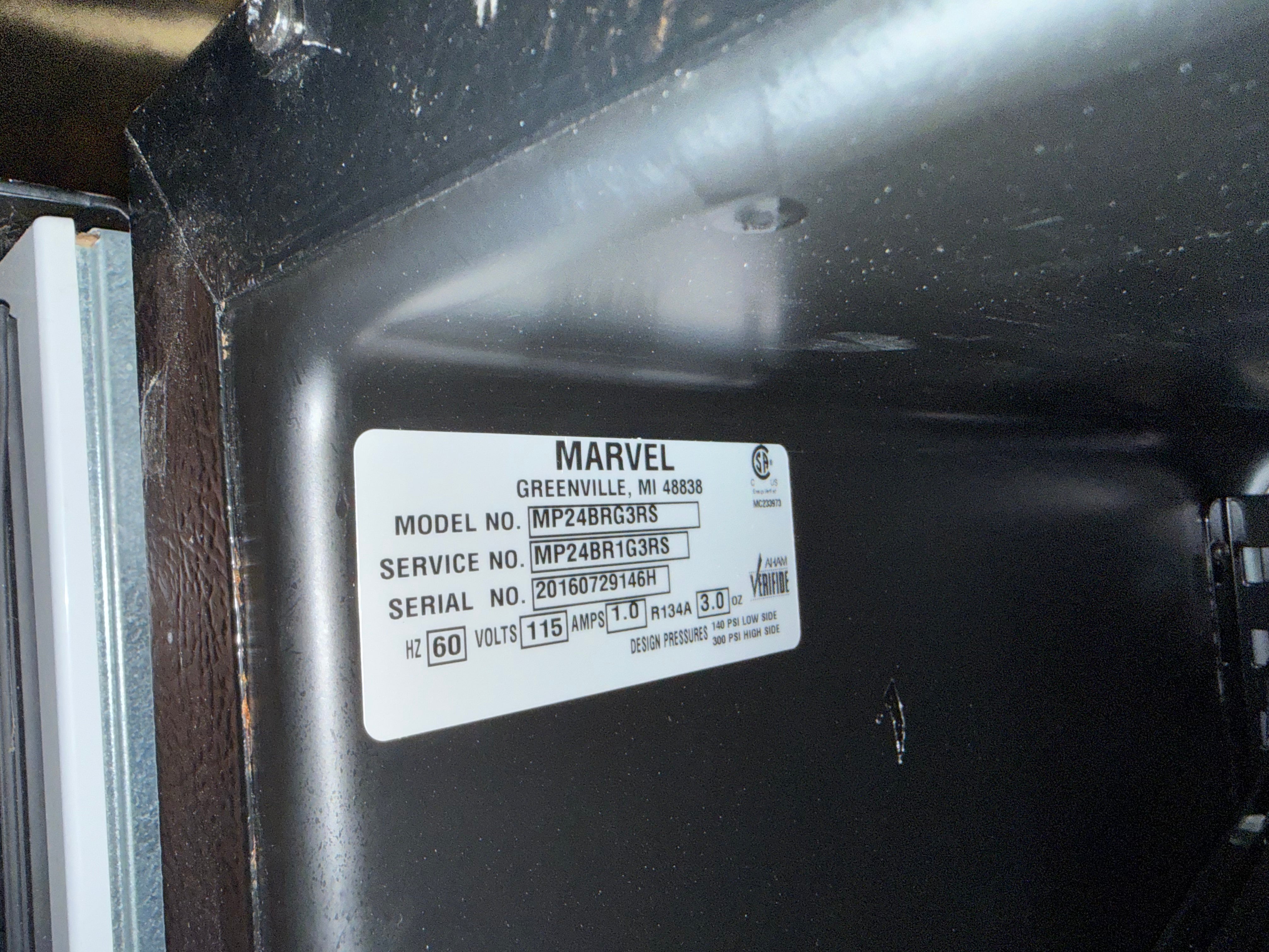 A close-up of a white Marvel product label on the inside of a black appliance door, showing model and serial information.