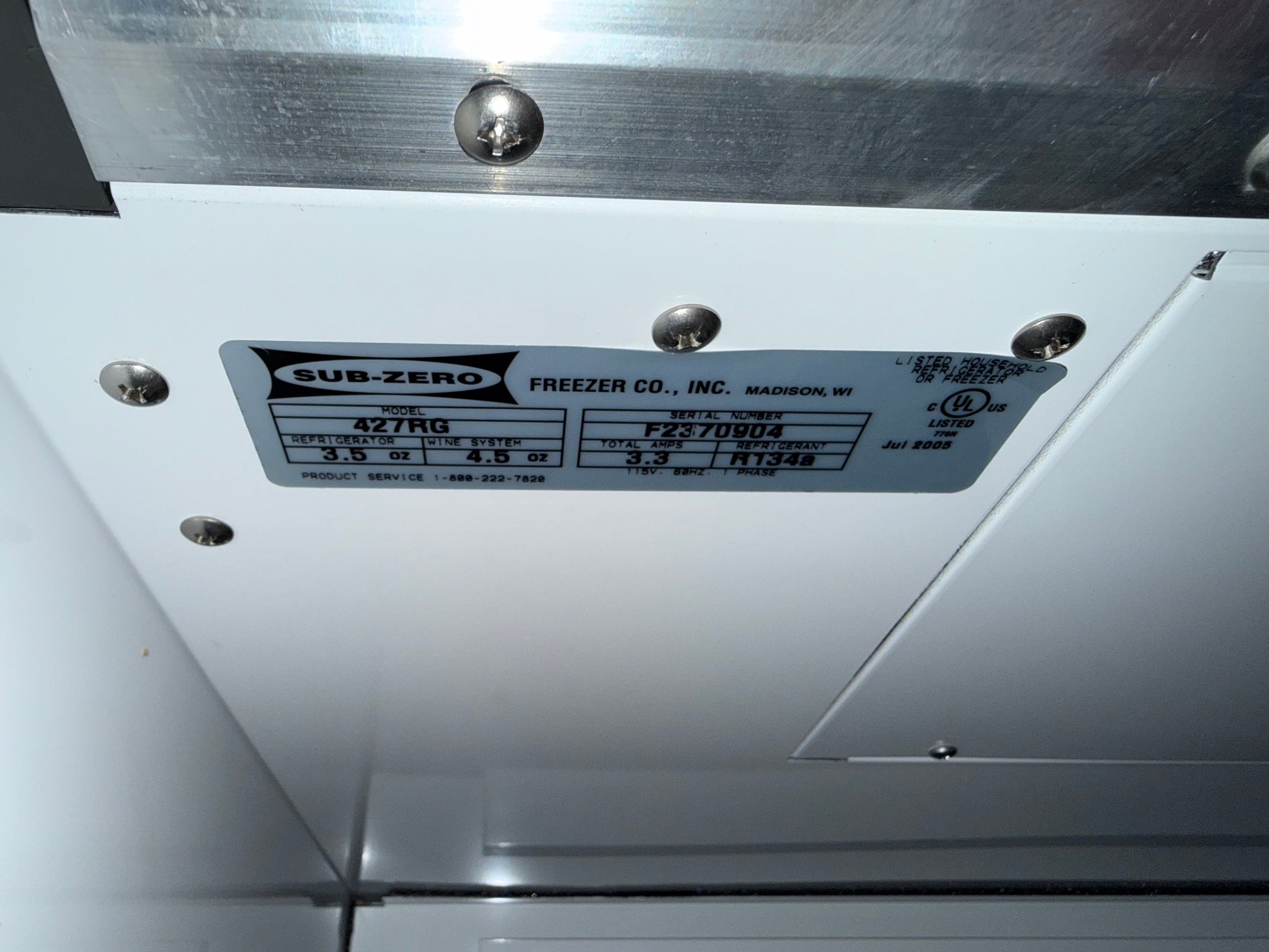 A close-up of a Sub-Zero freezer manual label attached to a white metal panel with screws, showing product specifications.