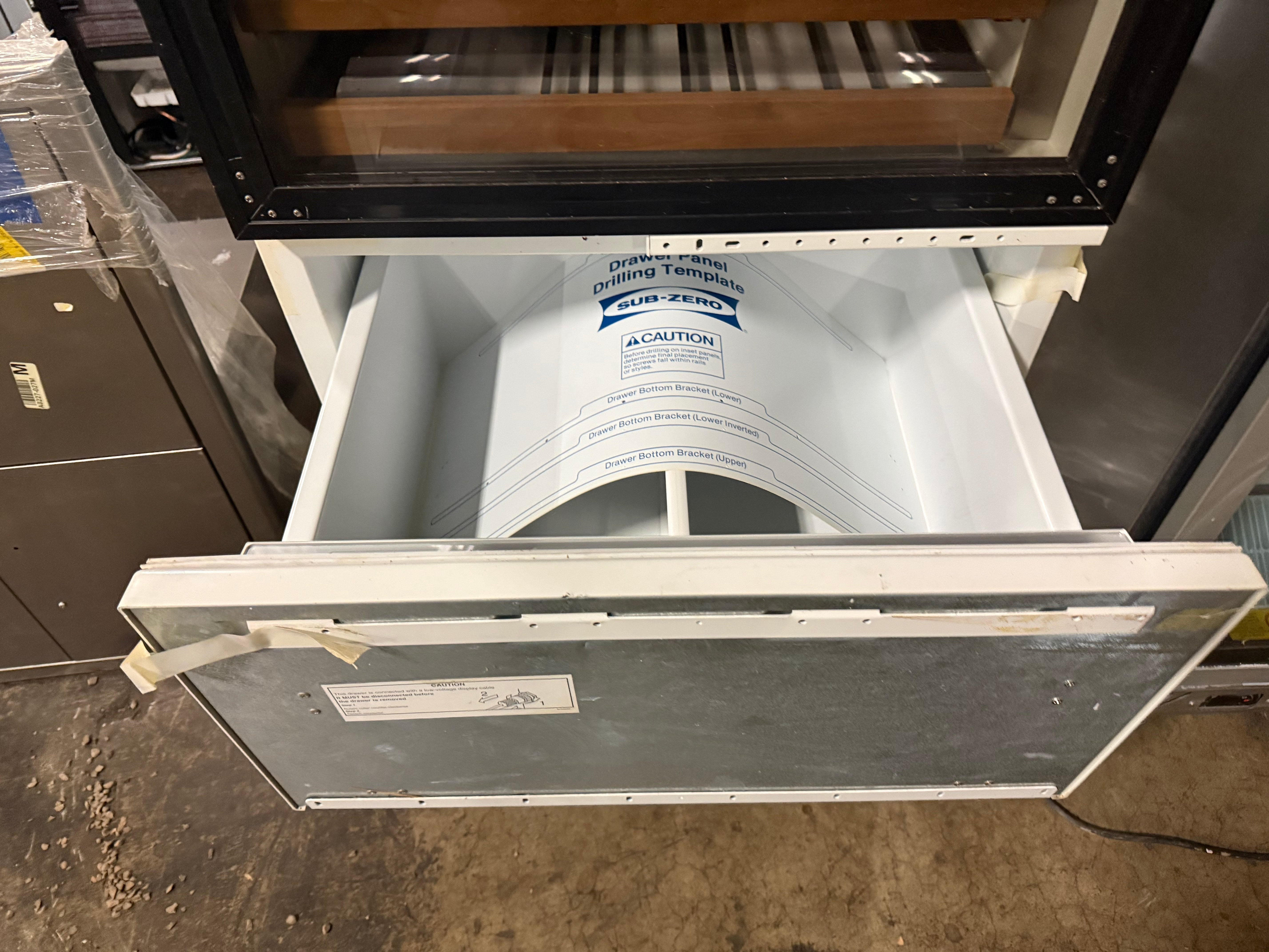 An open white and silver refrigerator door showing the interior shelves and a paper liner inside, photographed in a warehouse or storage area.