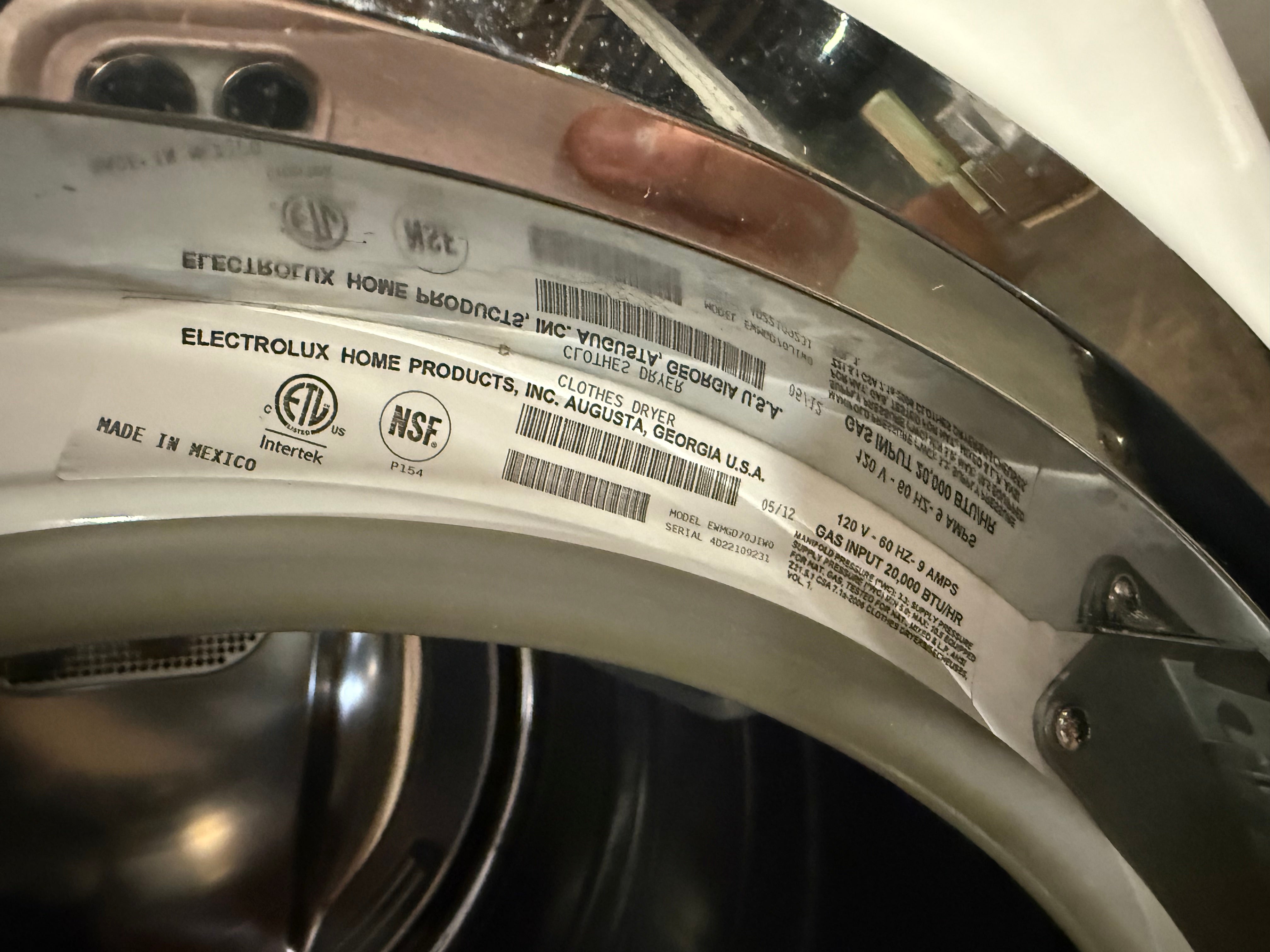 A close-up of a washing machine drum interior showing a large white product warranty label with barcodes and text, including Electrolux Home Products and NSF certification marks.