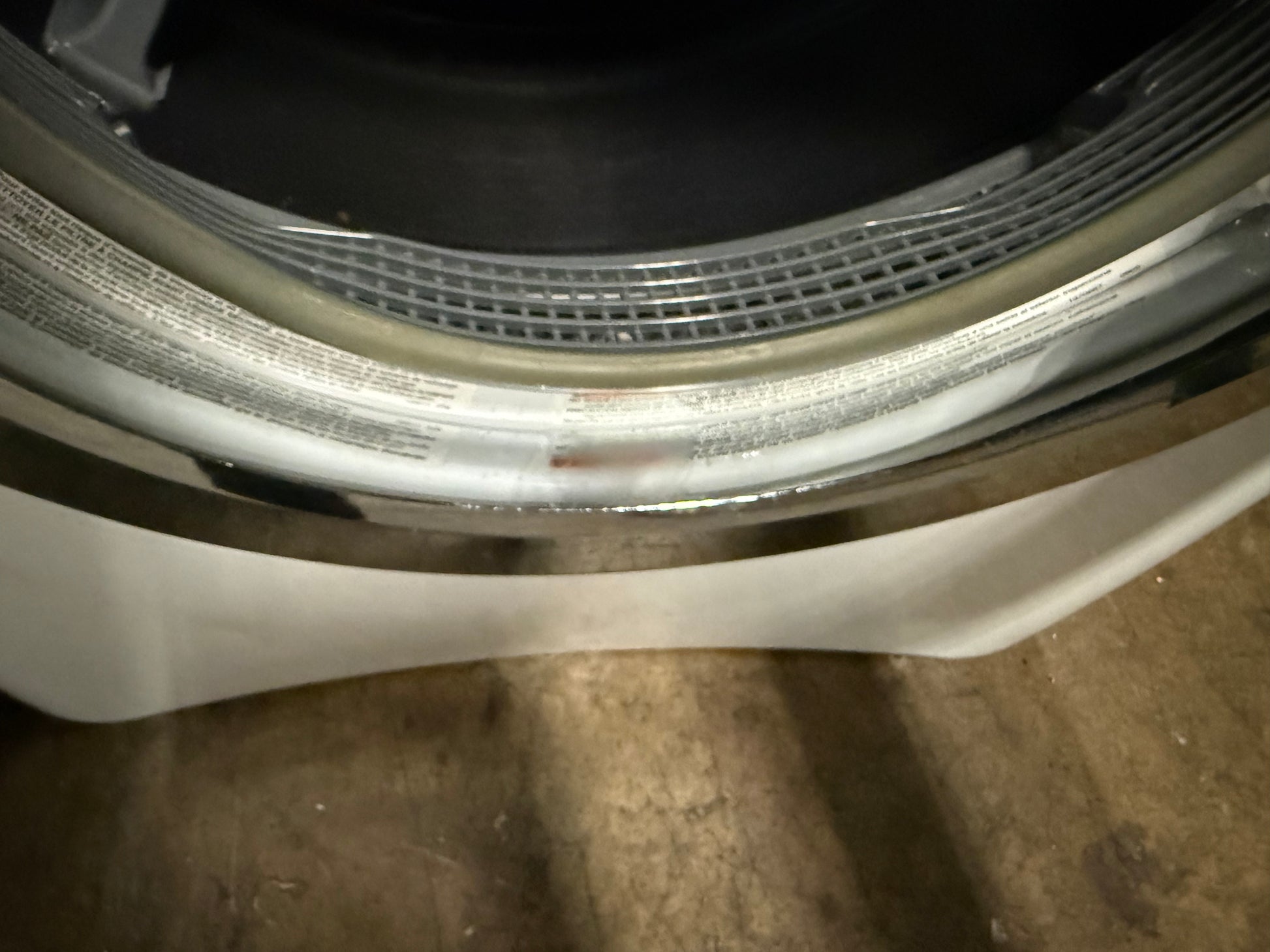 Close-up of the inner door seal and rubber gasket area of a front-loading washing machine, showing the silver metal rim, translucent door seal, and white drum interior.