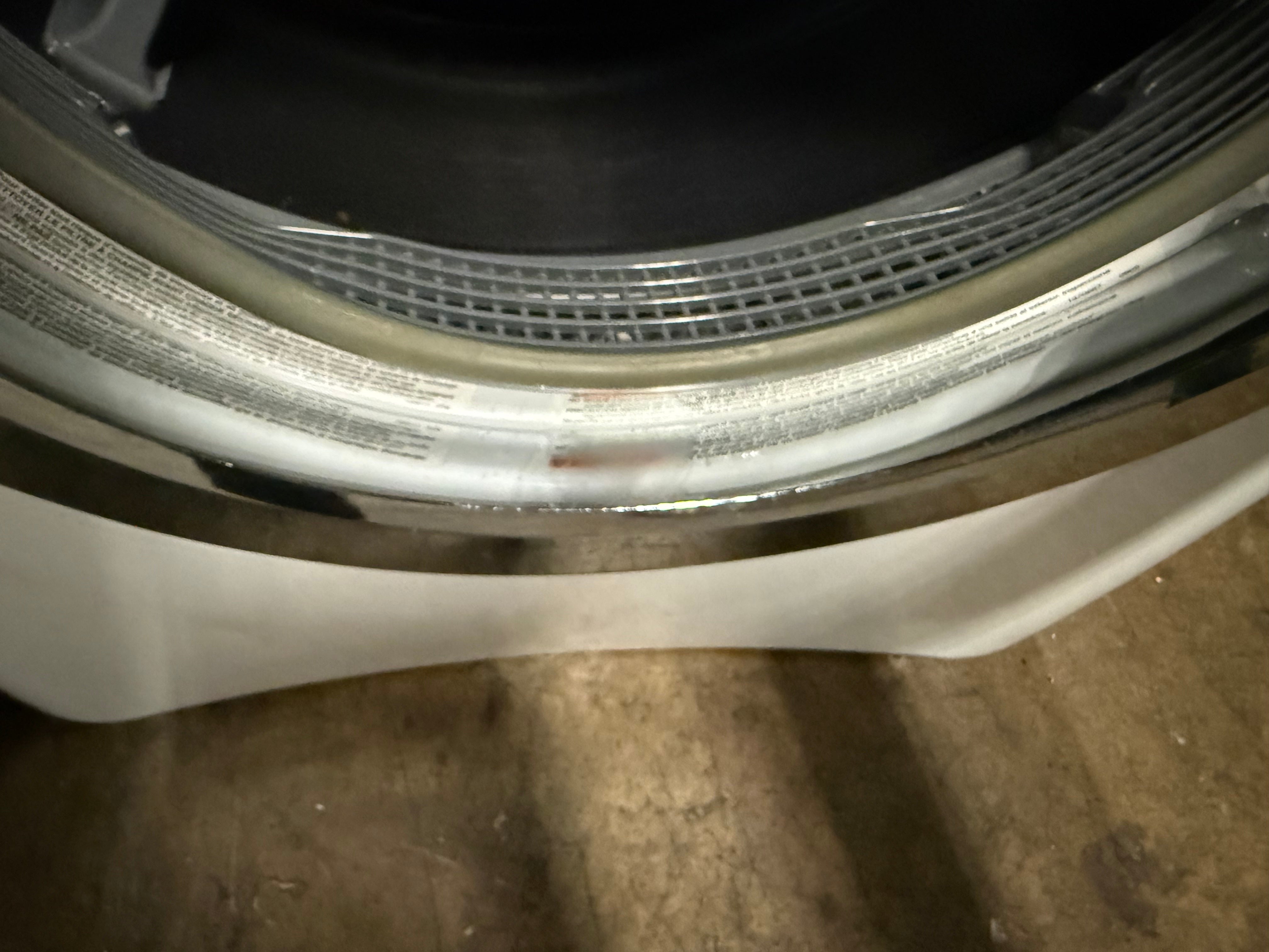 Close-up of the inner door seal and rubber gasket area of a front-loading washing machine, showing the silver metal rim, translucent door seal, and white drum interior.