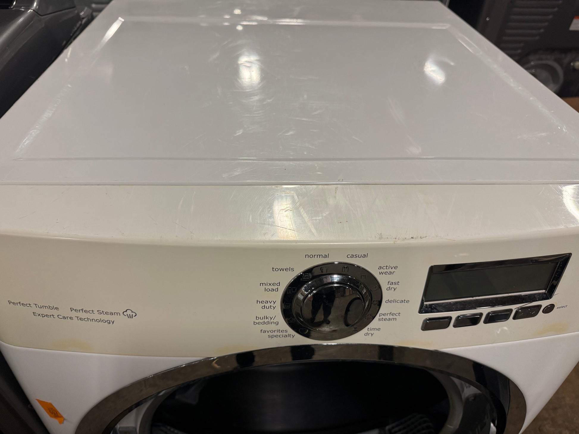 A white front-loading washing machine with a black control dial and digital display screen, photographed from a front-facing angle.
