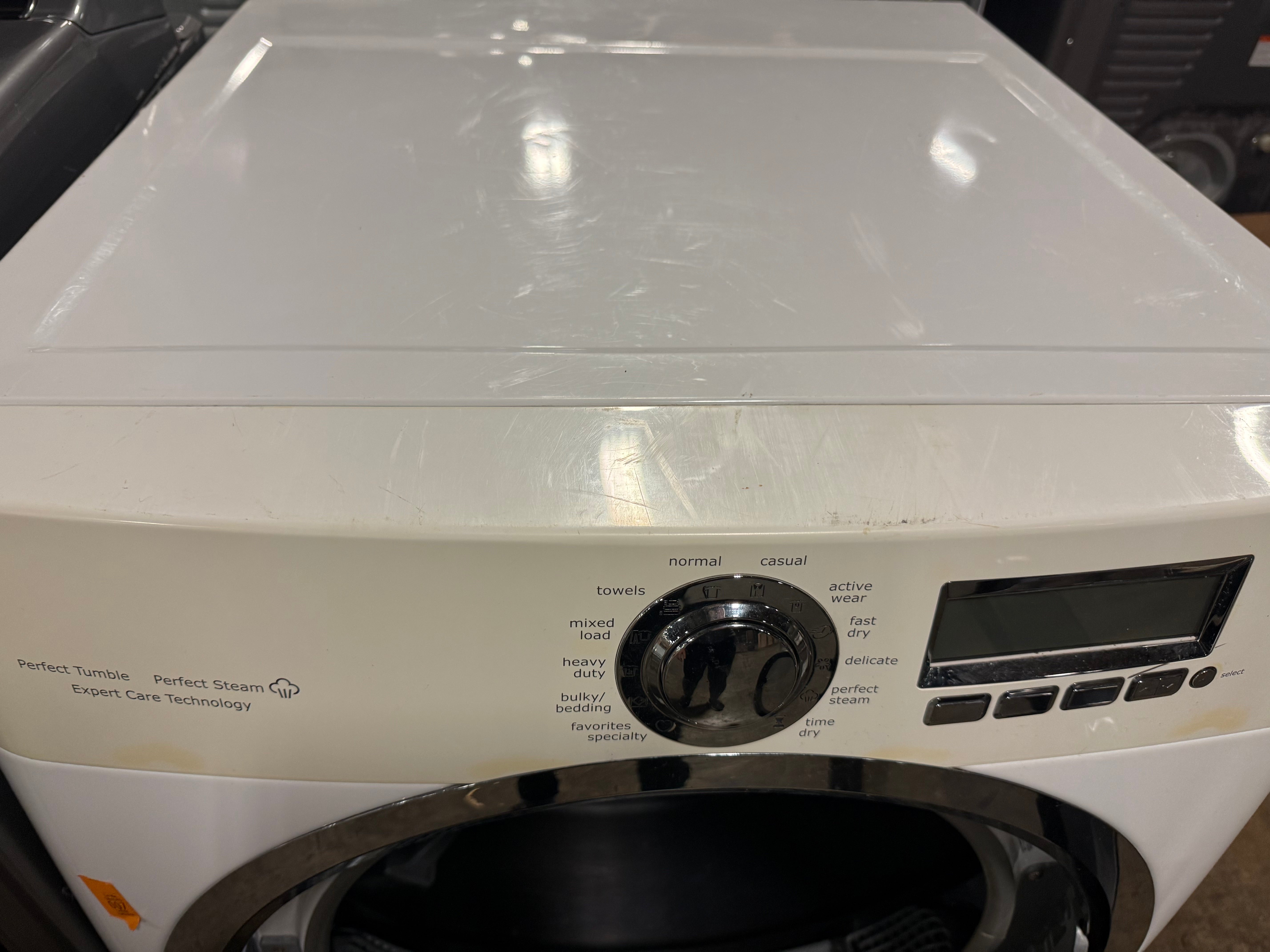 A white front-loading washing machine with a black control dial and digital display screen, photographed from a front-facing angle.