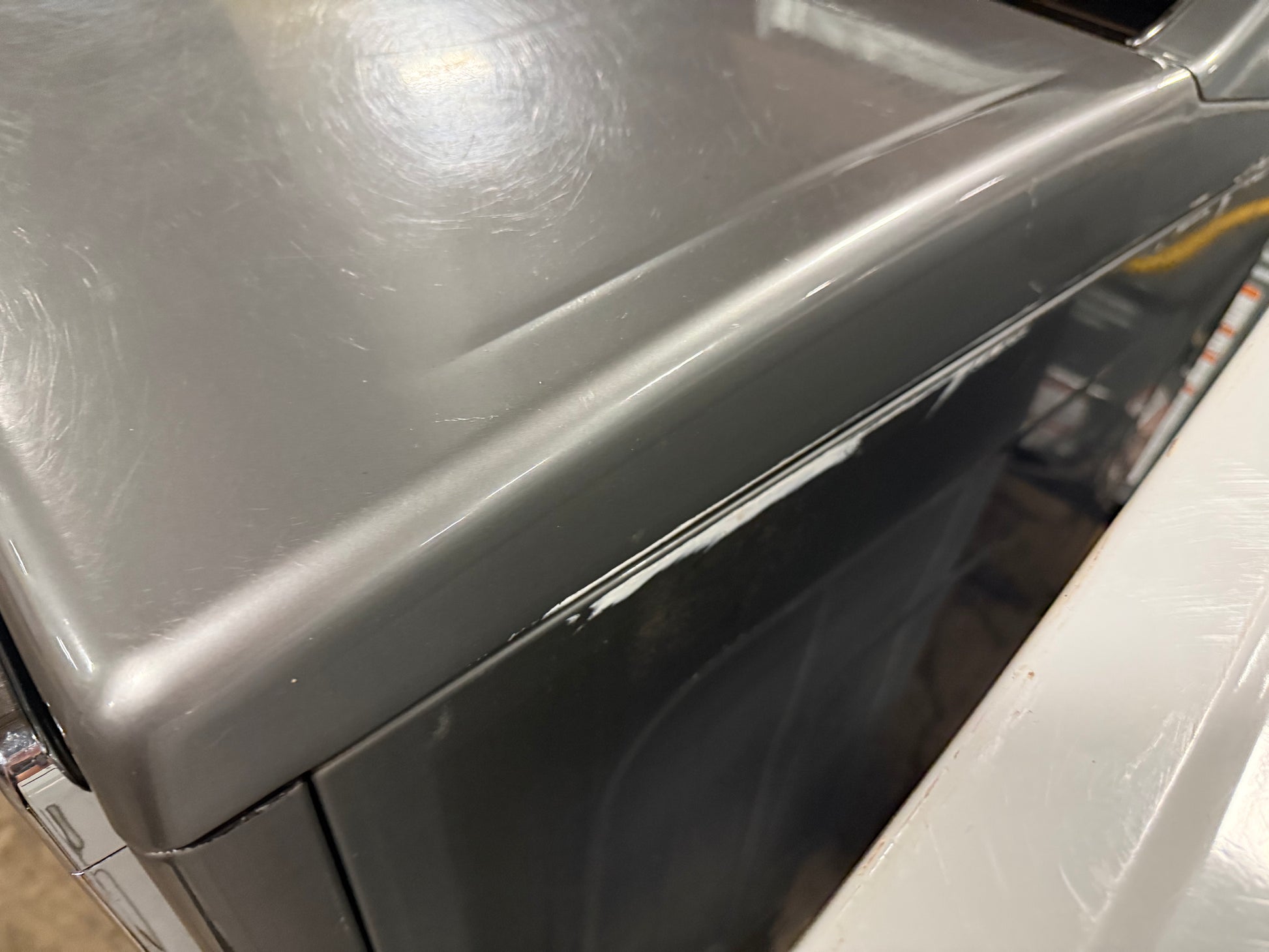 Close-up of a gray appliance, likely a washing machine or dryer, showing the top panel with visible scratches and scuffs, alongside a white unit next to it.