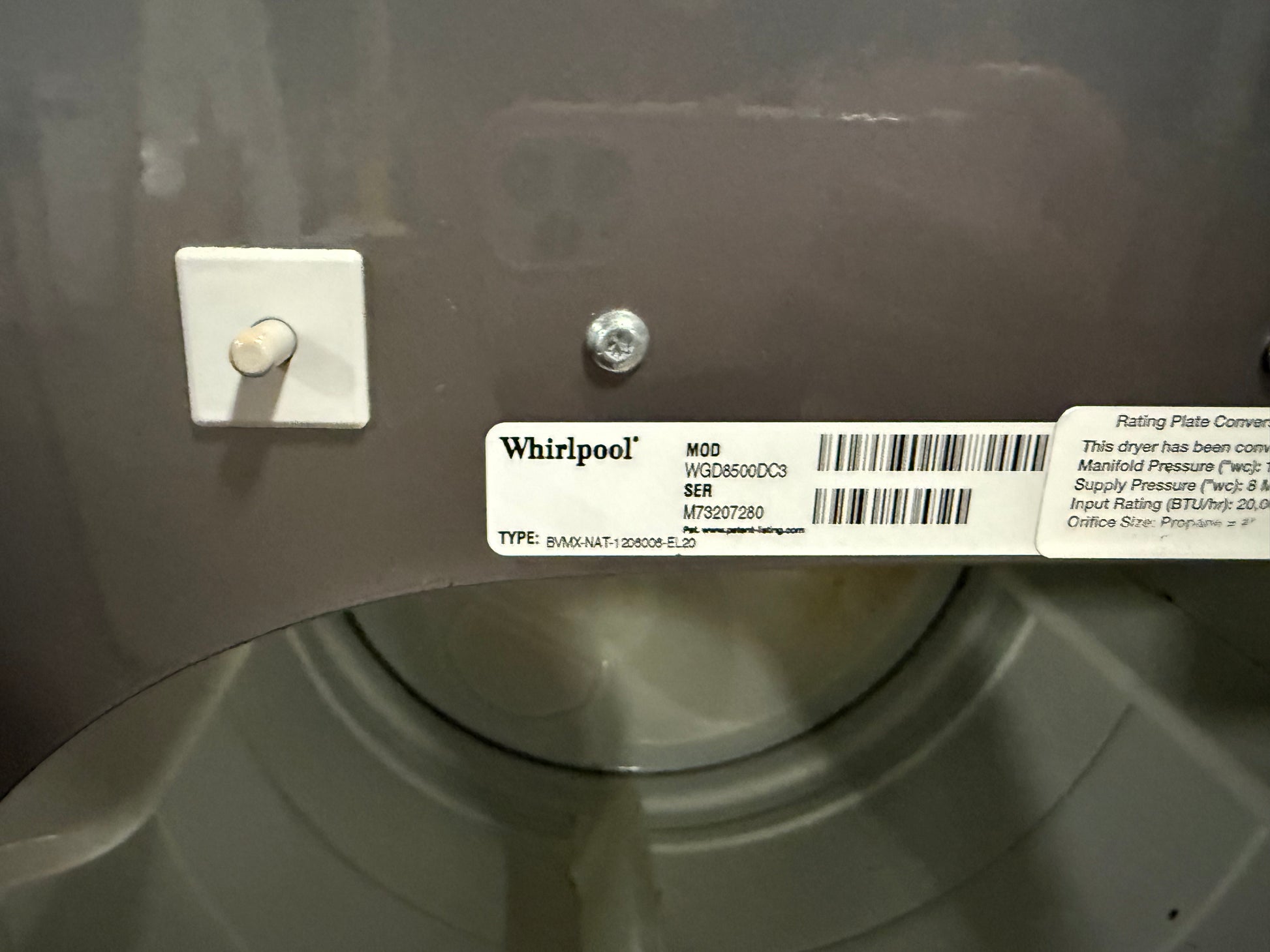 A close-up of a Whirlpool appliance interior or drum area showing a product label with model information and a white wall-mounted switch.