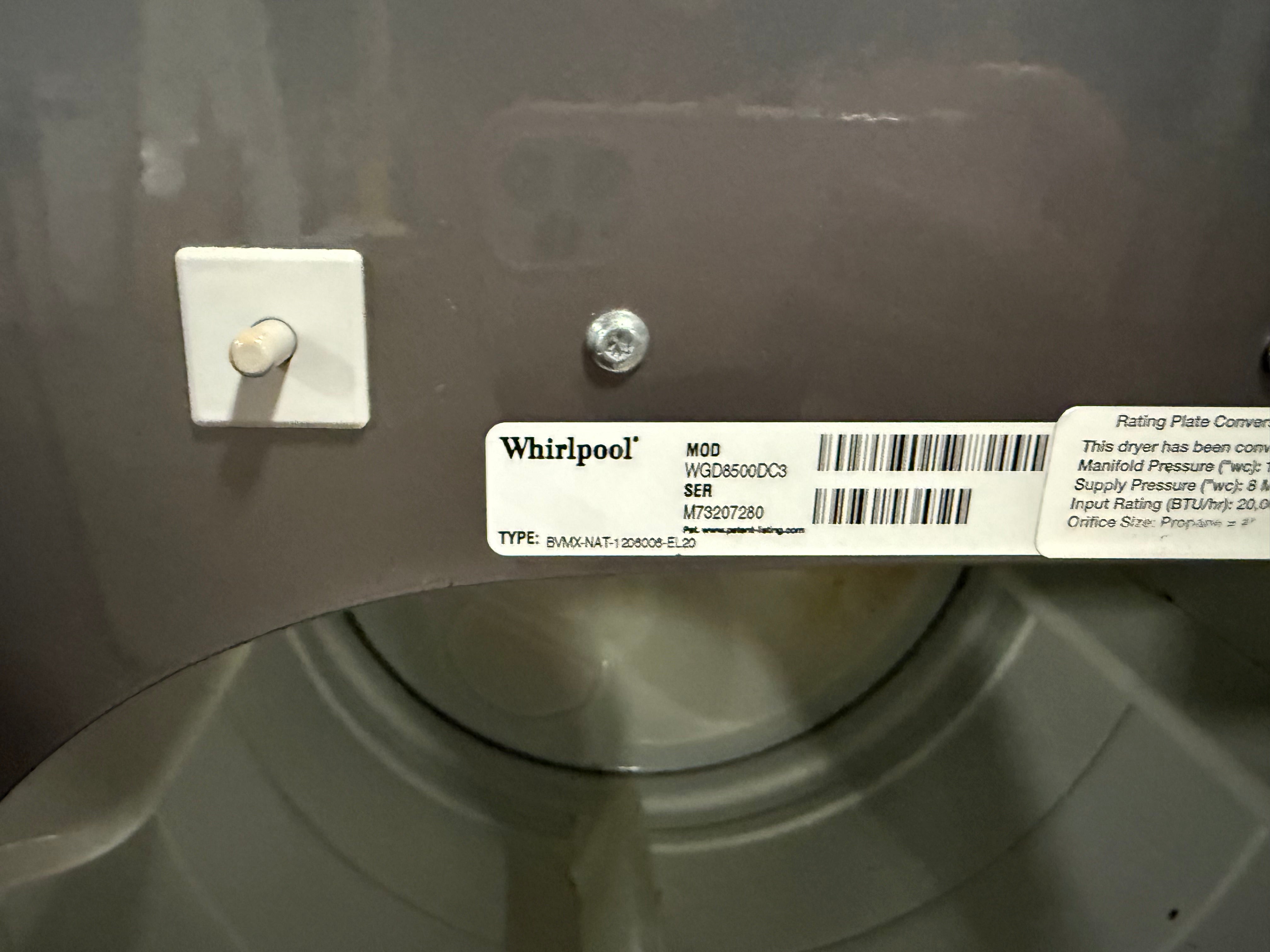 A close-up of a Whirlpool appliance interior or drum area showing a product label with model information and a white wall-mounted switch.