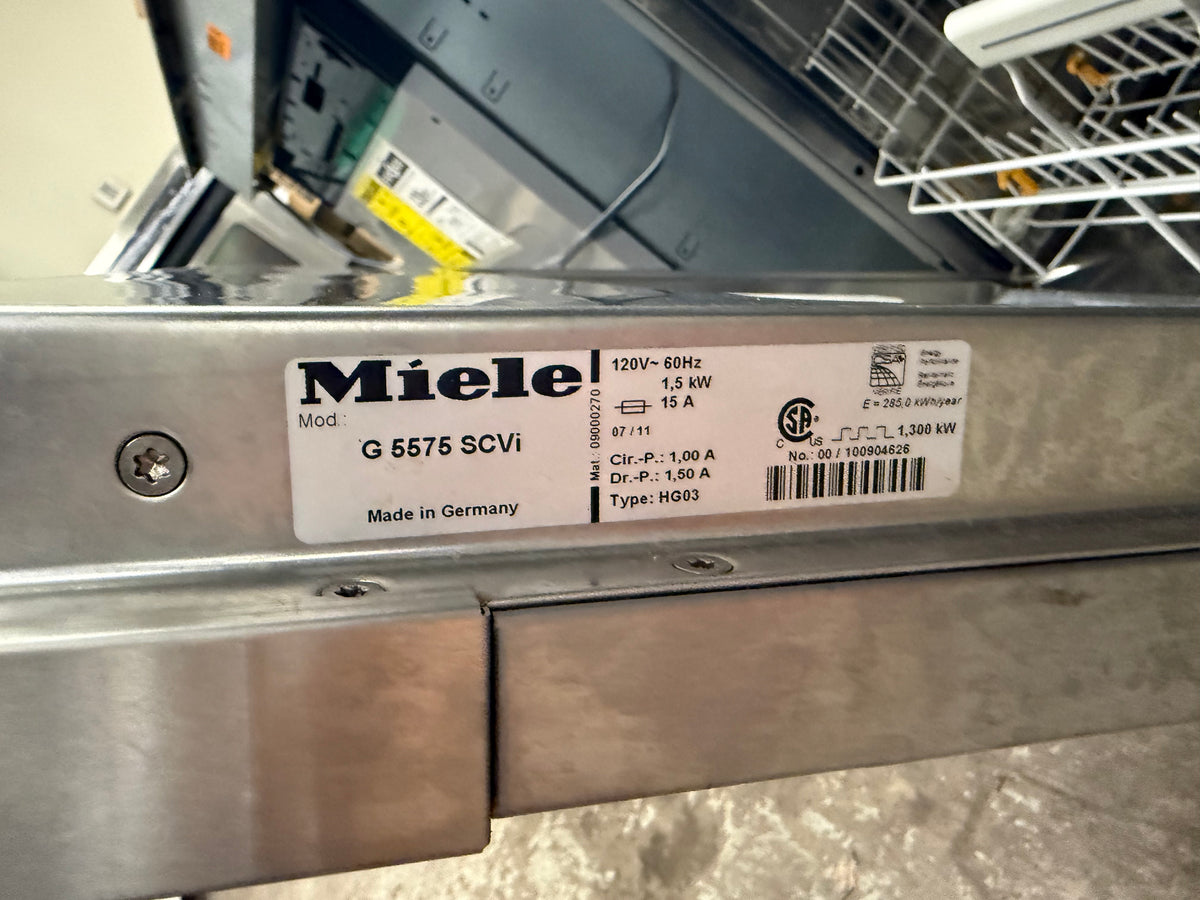A close-up of a stainless steel dishwasher showing a white Miele product label with model details G 5575 SCVI.