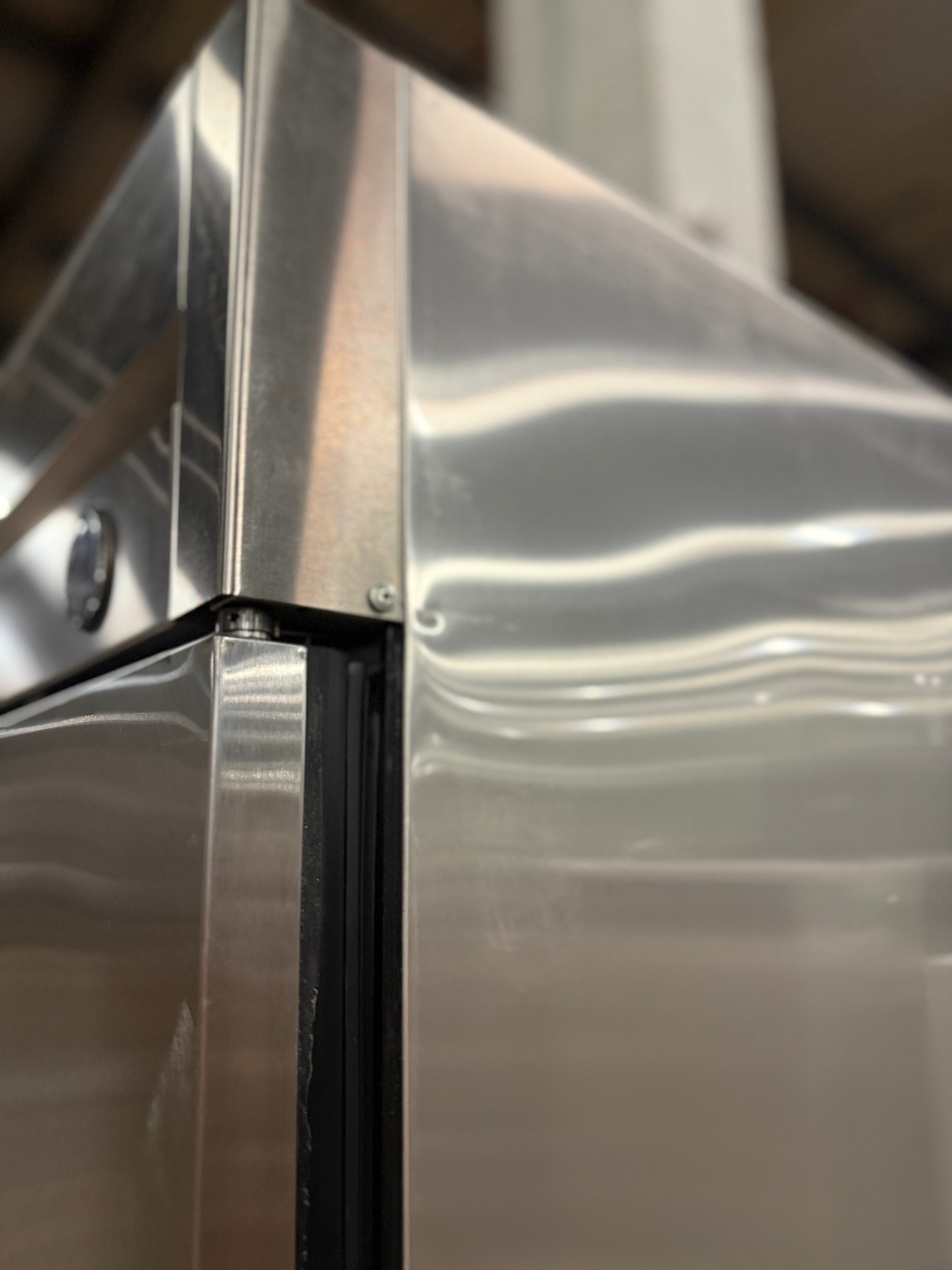 Close-up of a stainless steel appliance, showing the brushed metal surface, corner seam, and a black rubber gasket.