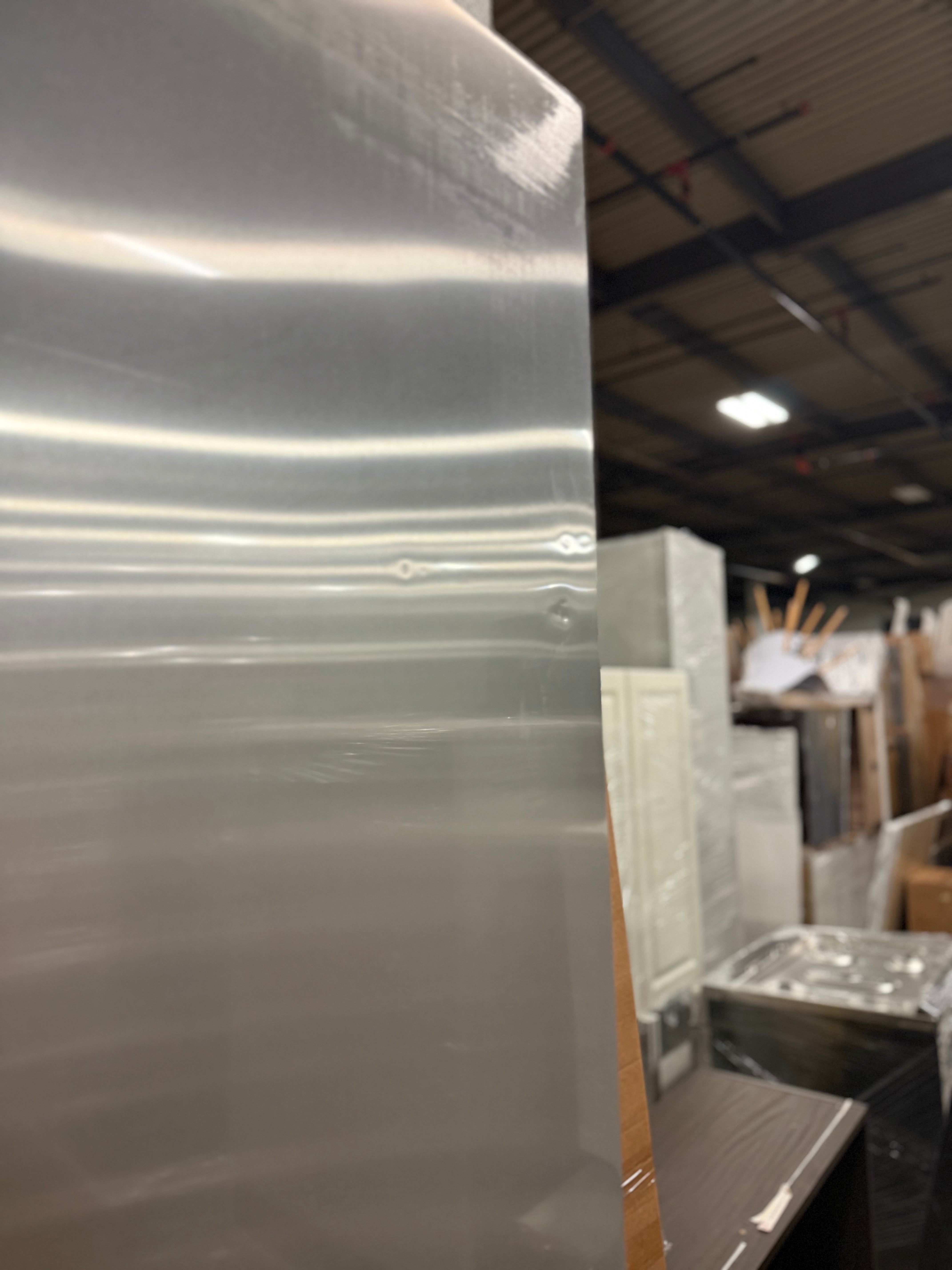 A large, unfinished sheet of brushed silver metal, likely stainless steel or aluminum, standing vertically in a warehouse or showroom setting.