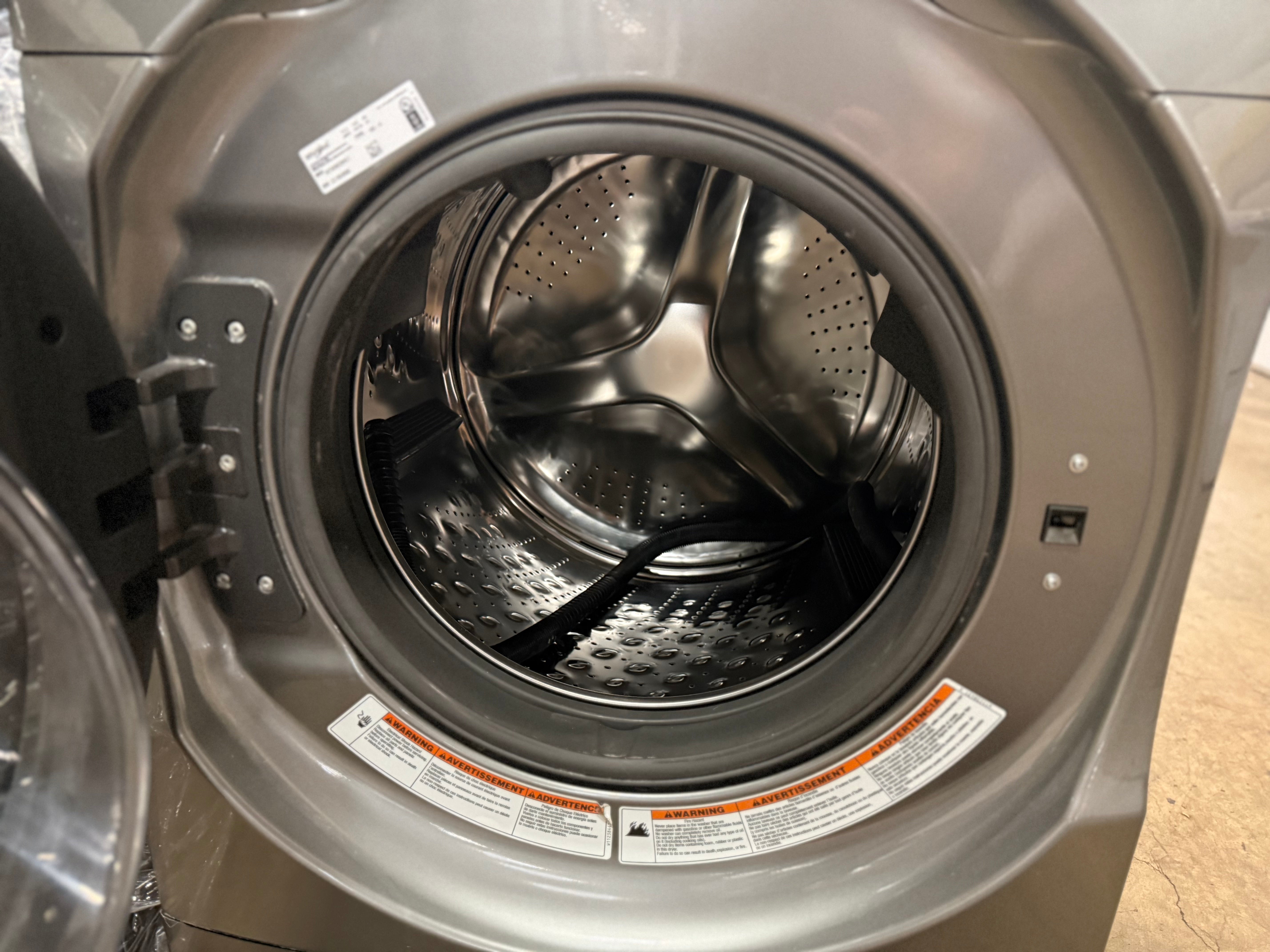 Close-up of the open front door and stainless steel drum of a front-loading washing machine.