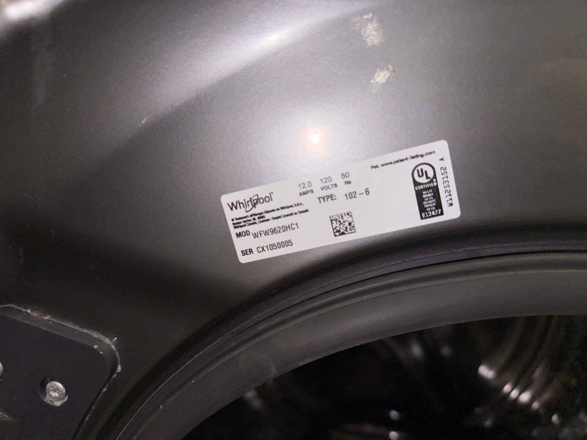 A close-up shot of a white Whirlpool product label on the dark gray curved body of a washing machine.