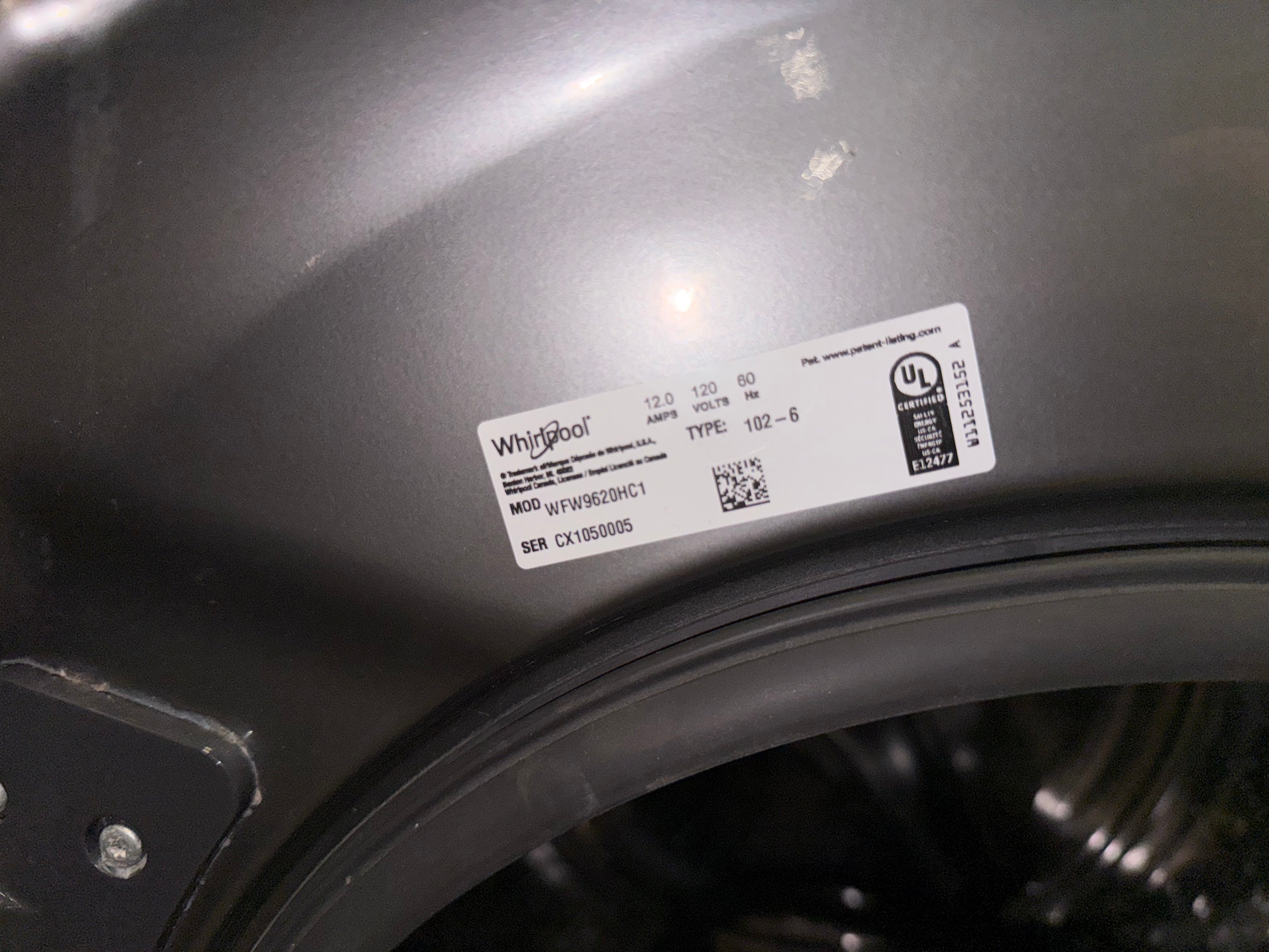 A close-up shot of a white Whirlpool product label on the dark gray curved body of a washing machine.
