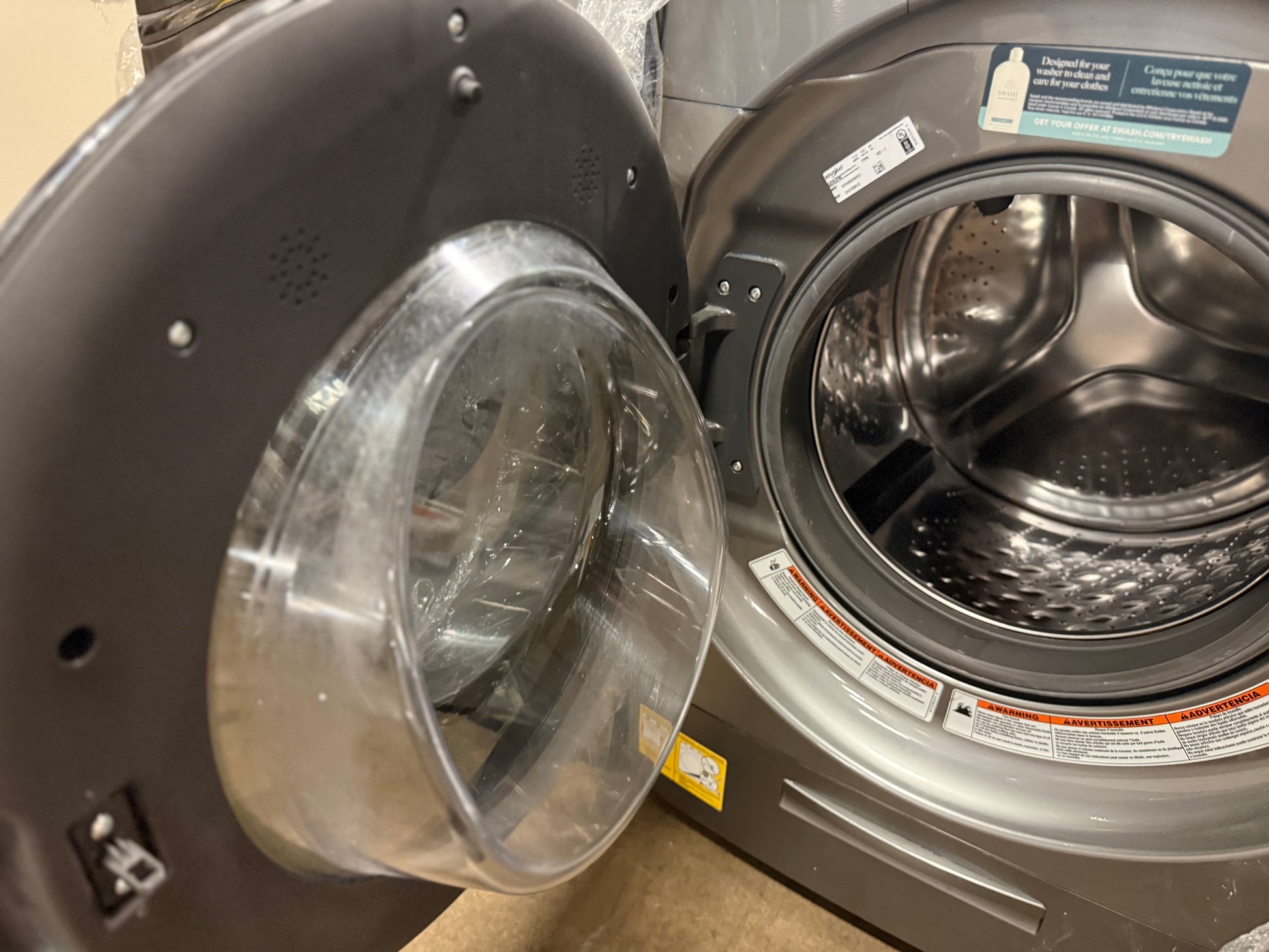 A close-up of a front-load washing machine with the door open, showing the transparent circular door seal and the stainless steel drum inside.
