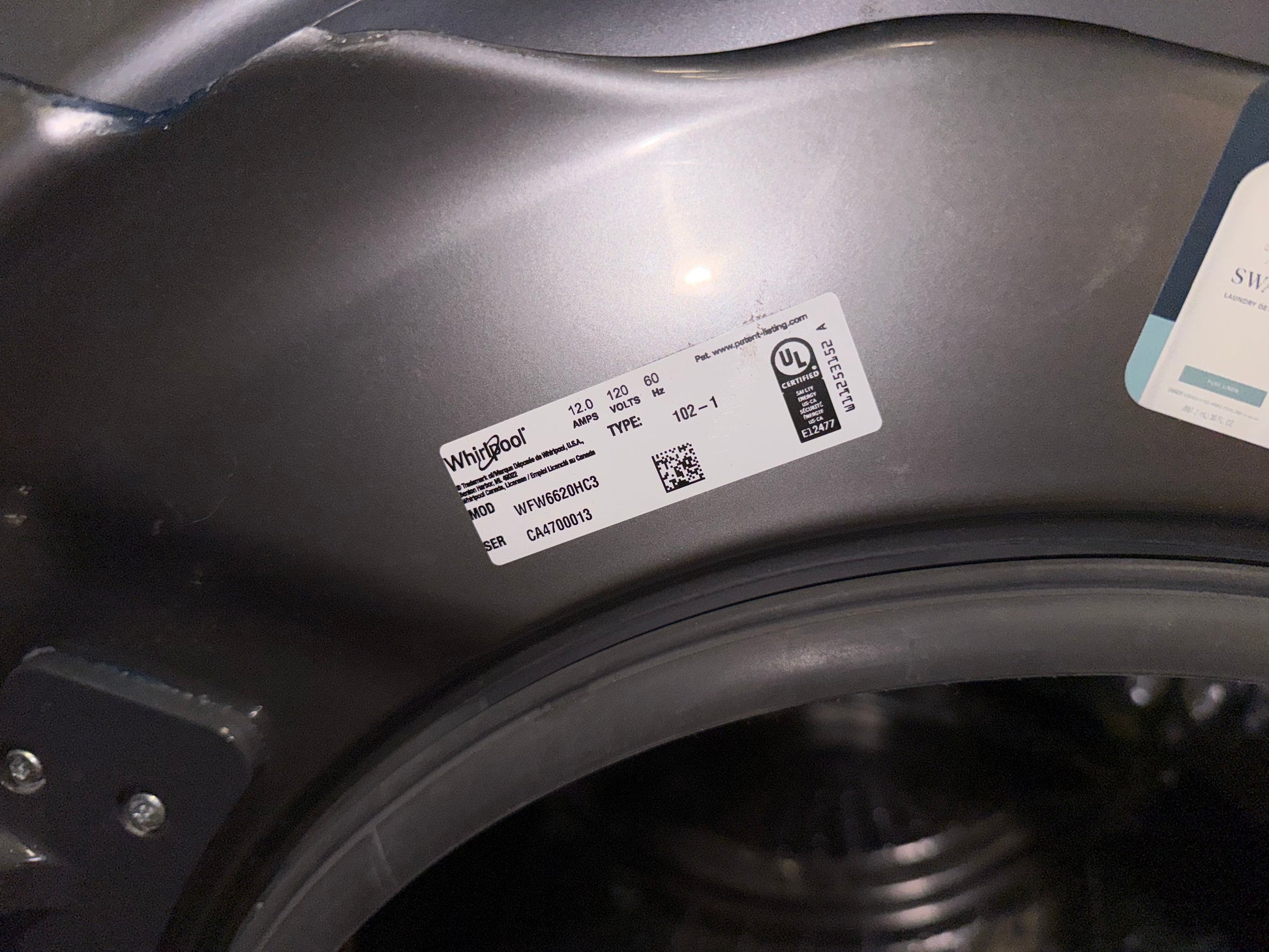 A close-up of a dark gray appliance interior, likely a washing machine drum opening, showing a white Whirlpool product label and a partial second label.