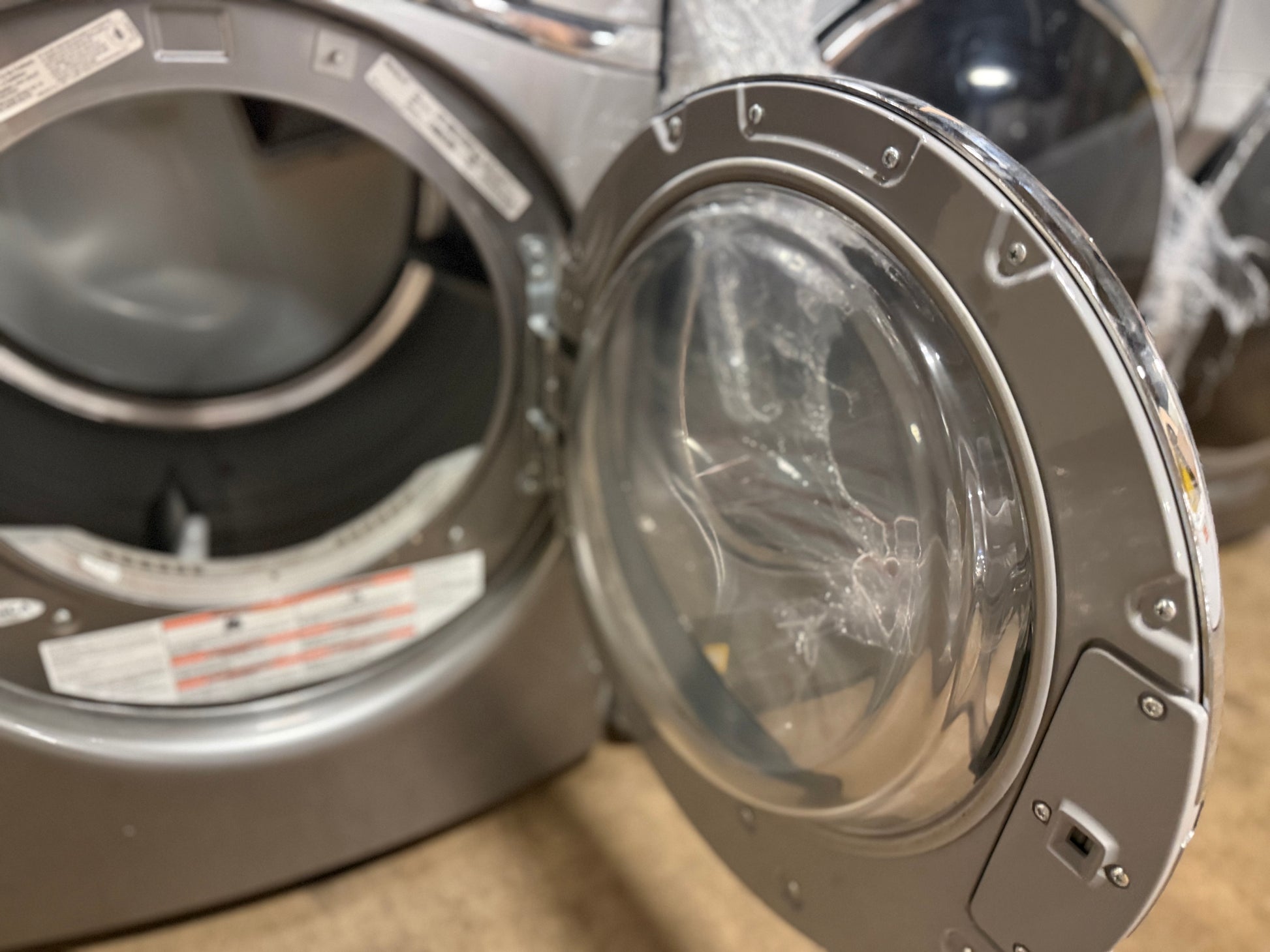 A close-up of a front-loading washing machine with the door open, showing the silver exterior, clear door, and inner drum.