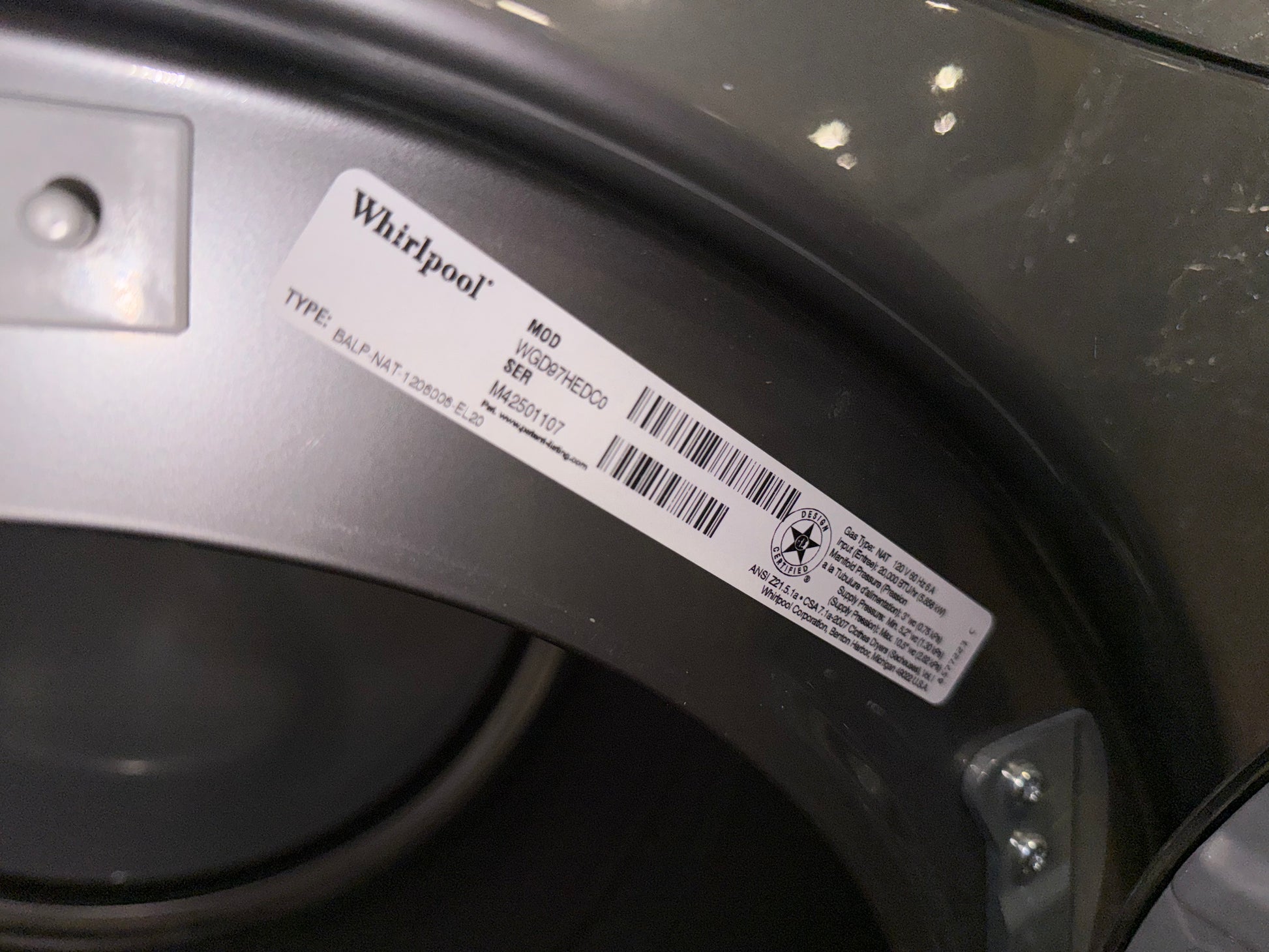 A close-up of a Whirlpool appliance label sticker on the inner silver and dark gray curved panel of a washing machine.